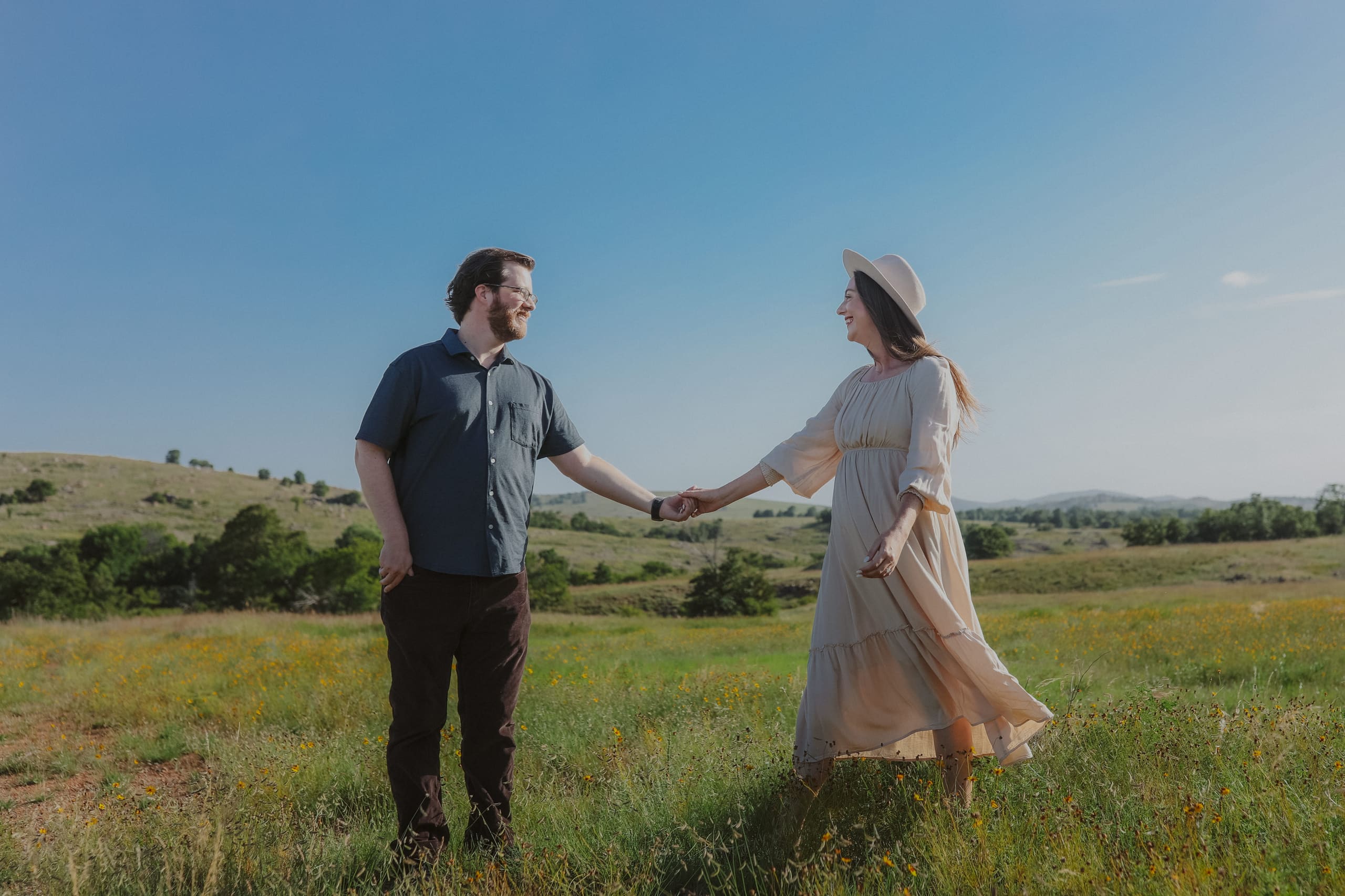 Hand in hand in a wildflower meadow, hills rolling away under a clear sky