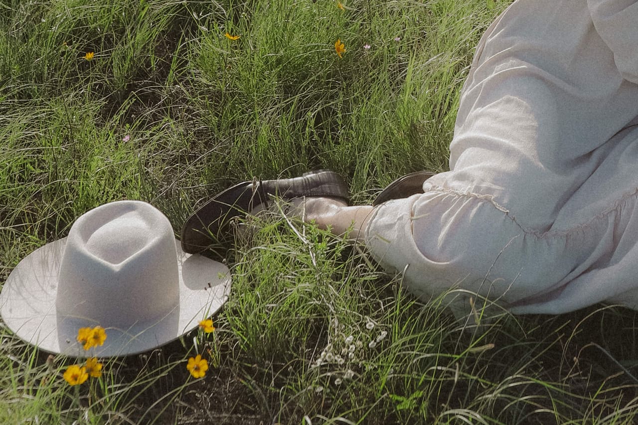 A hat resting in the grass beside her skirt and yellow wildflowers
