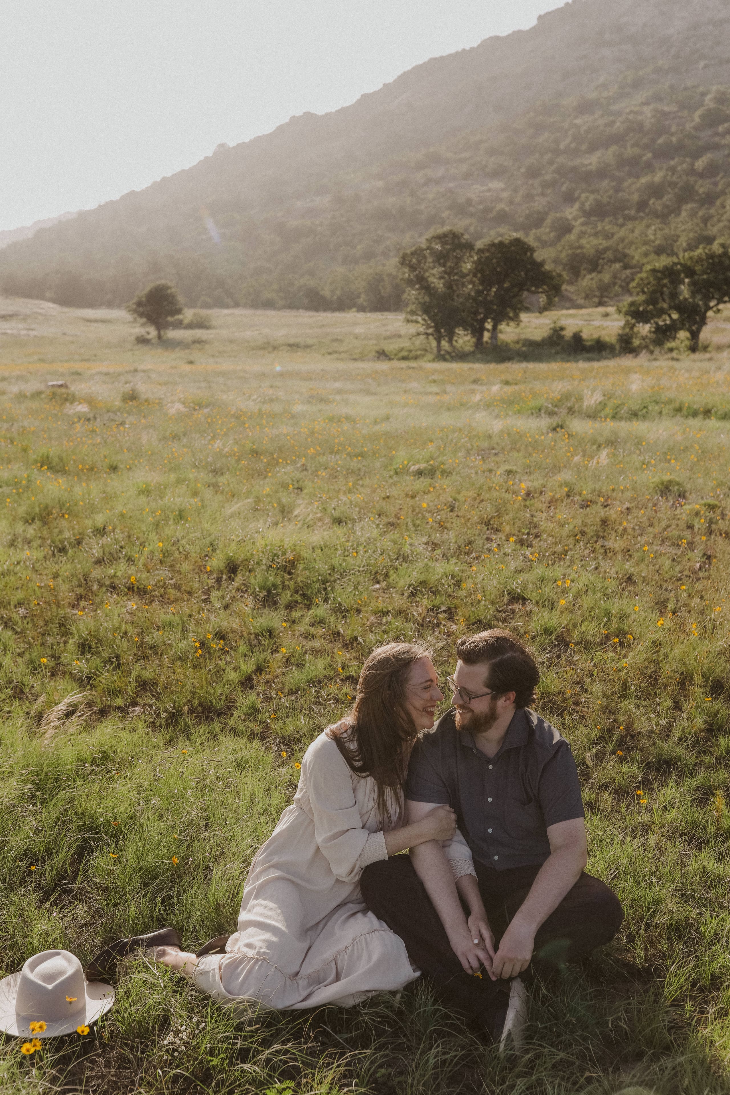 A close-up of her hands wrapped around his arm, the engagement ring catching the light