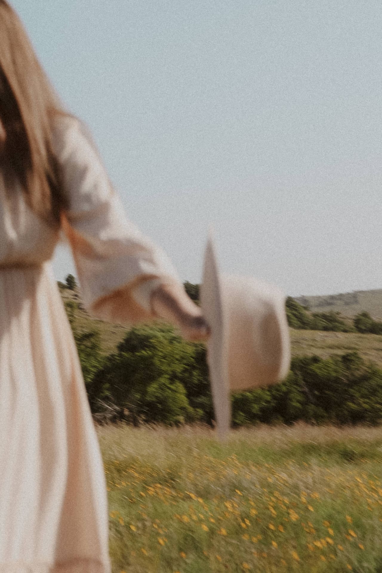 Hat swinging from her hand as she walks through the wildflowers