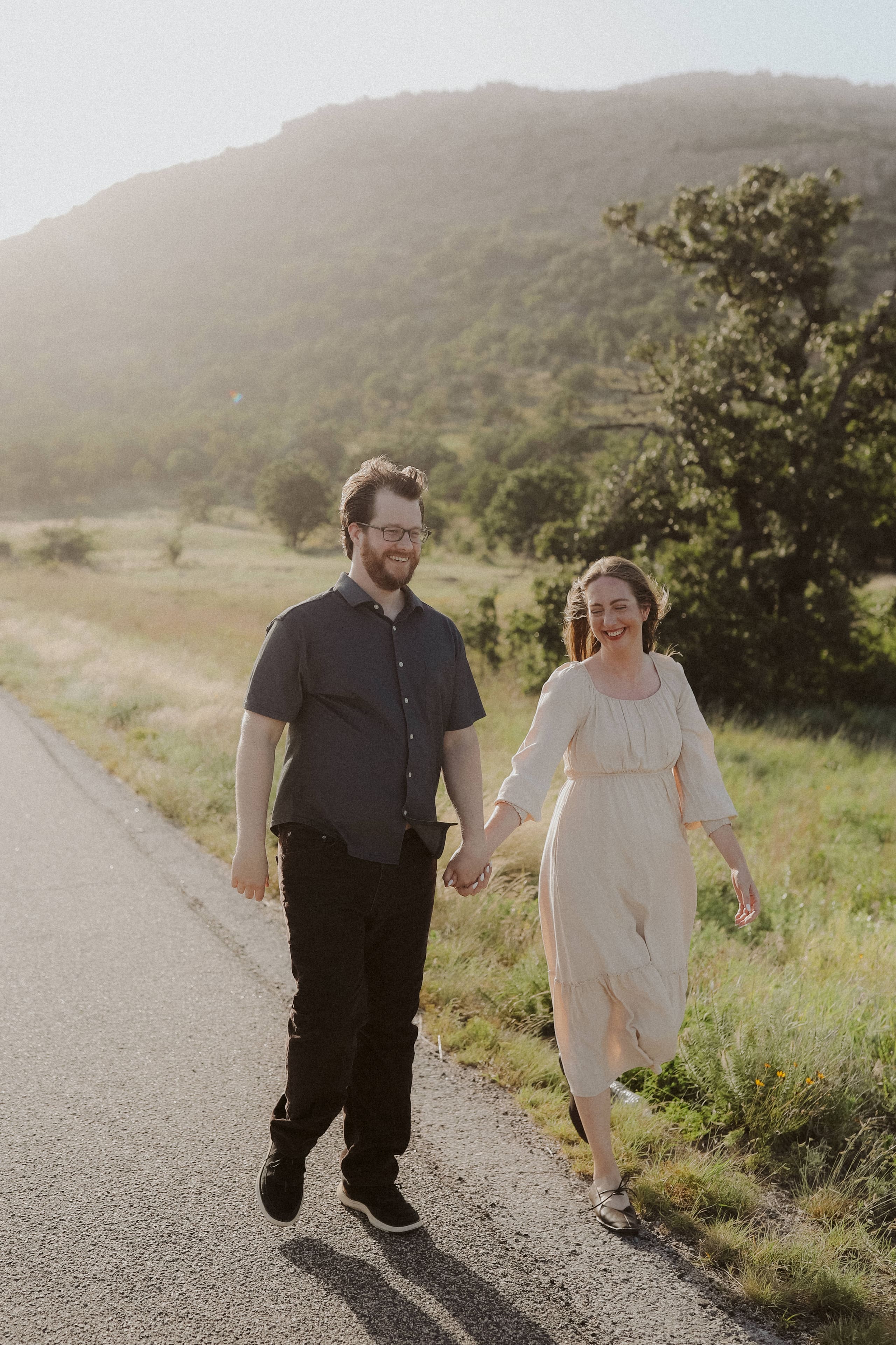 Laughing hand in hand along a sunlit road beneath the mountain