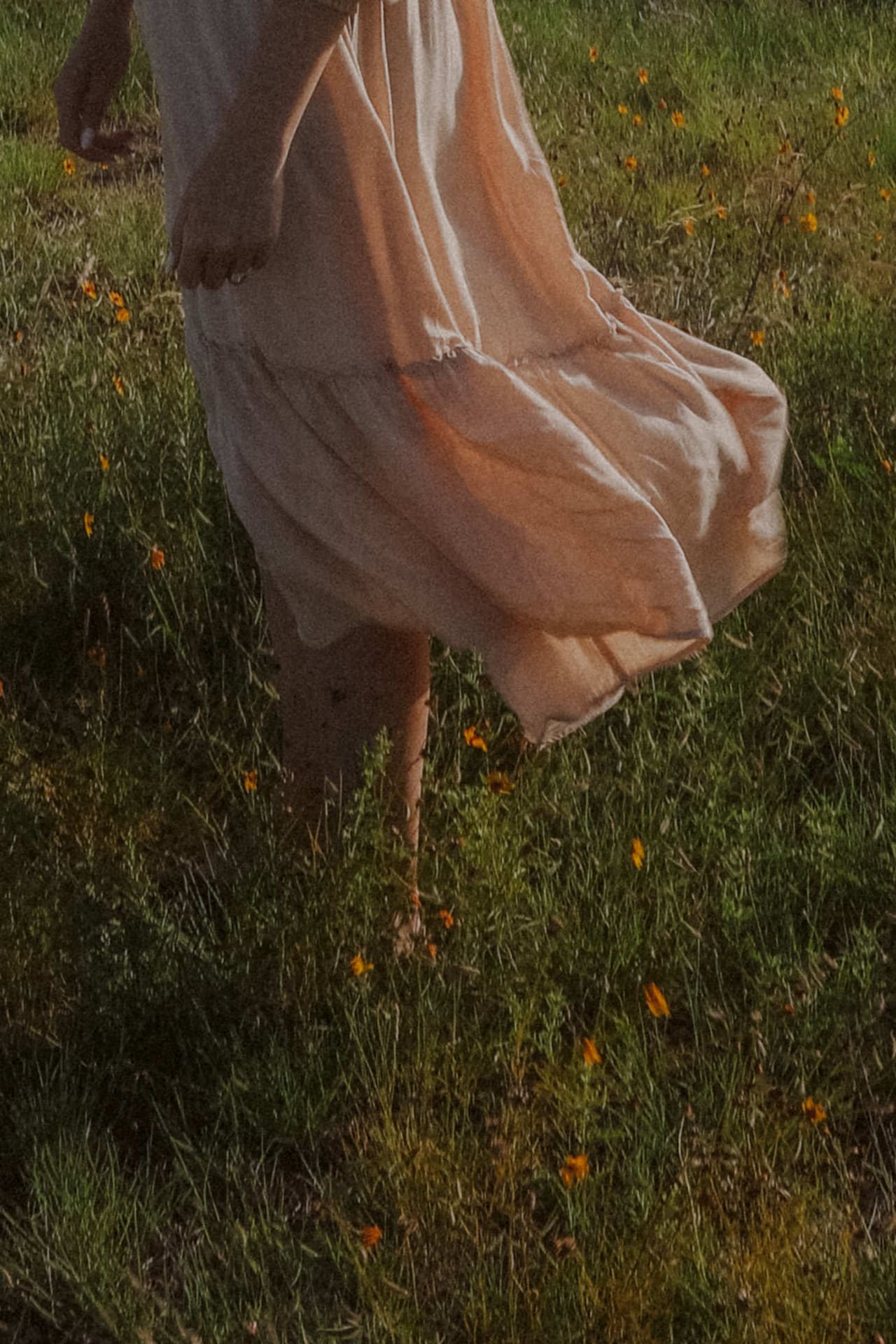 Her dress swirling barefoot through grass dotted with yellow wildflowers