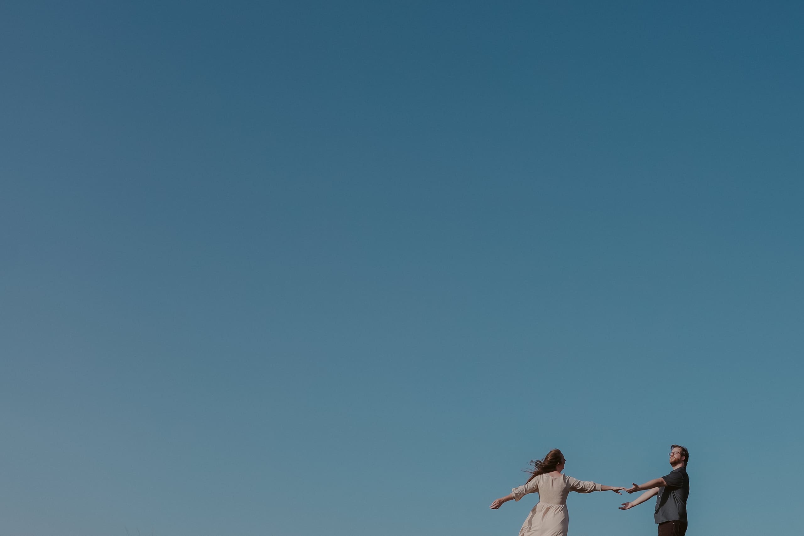 Arms outstretched toward each other under a deep blue sky