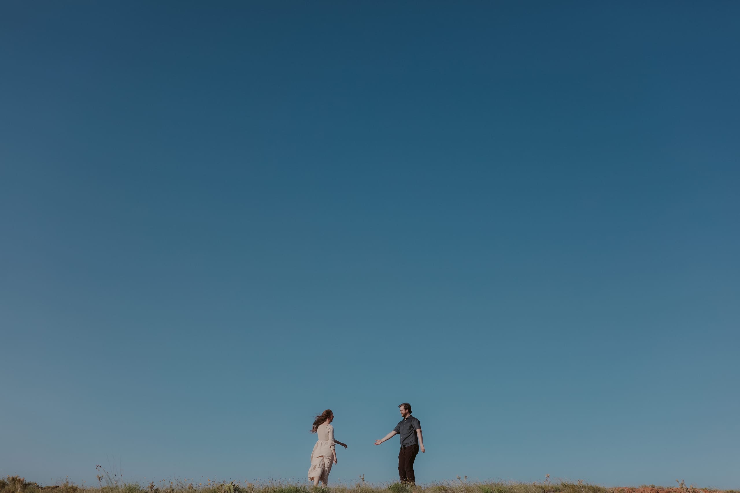 Stepping toward each other along the grassy ridge, sky filling the frame