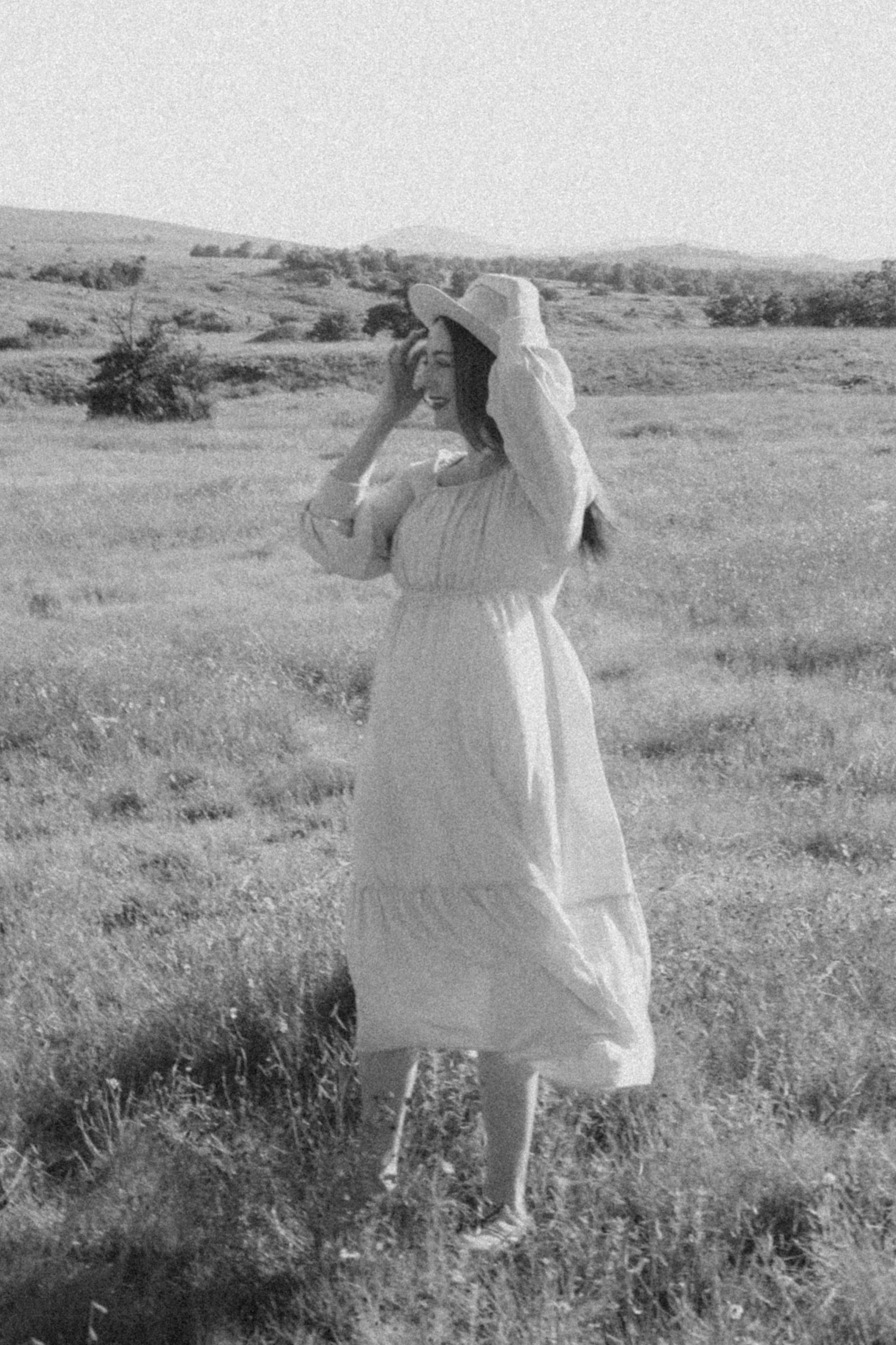 A black-and-white portrait — she holds her hat in a windswept field