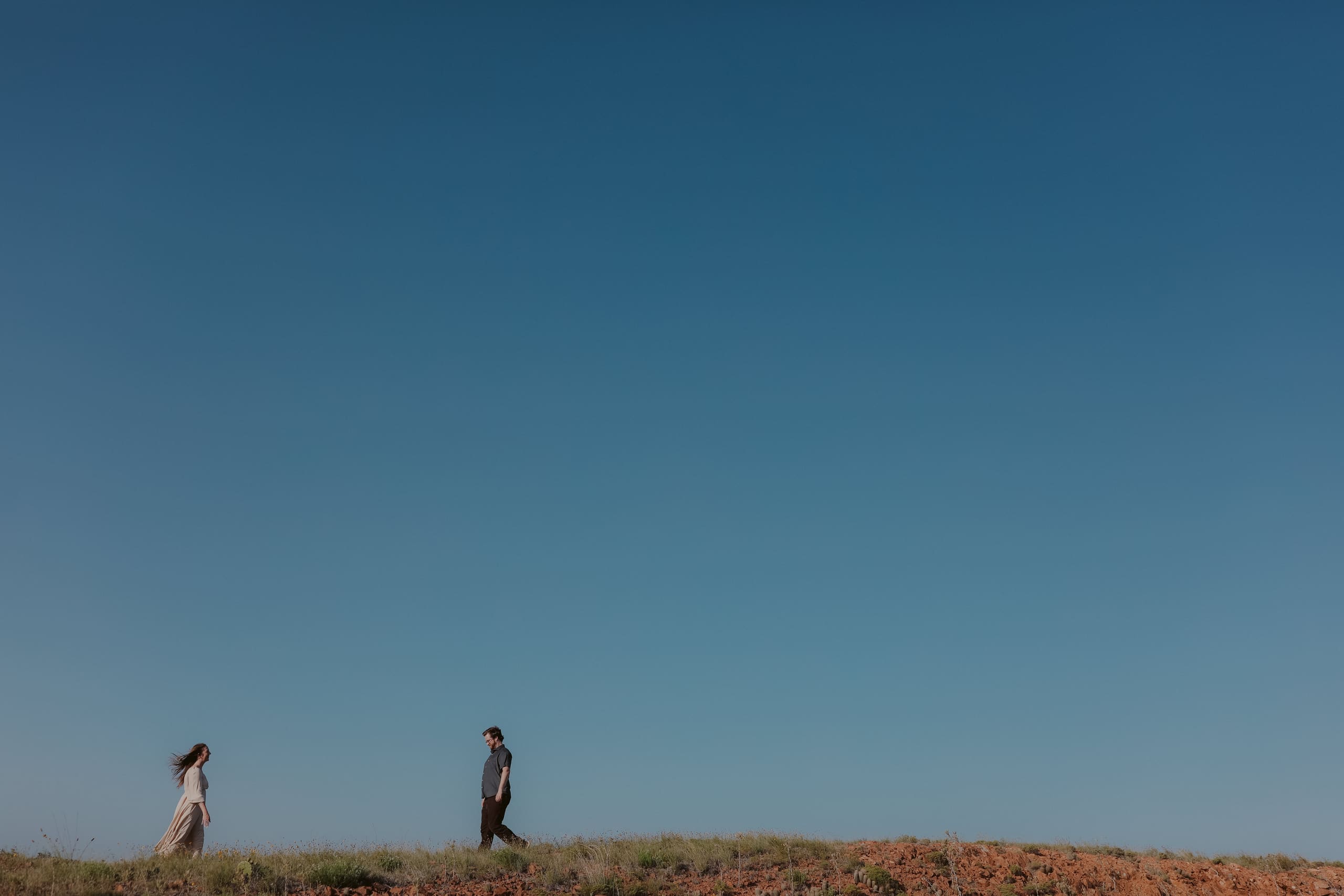 Two small figures crossing a grassy ridge under a wide blue sky