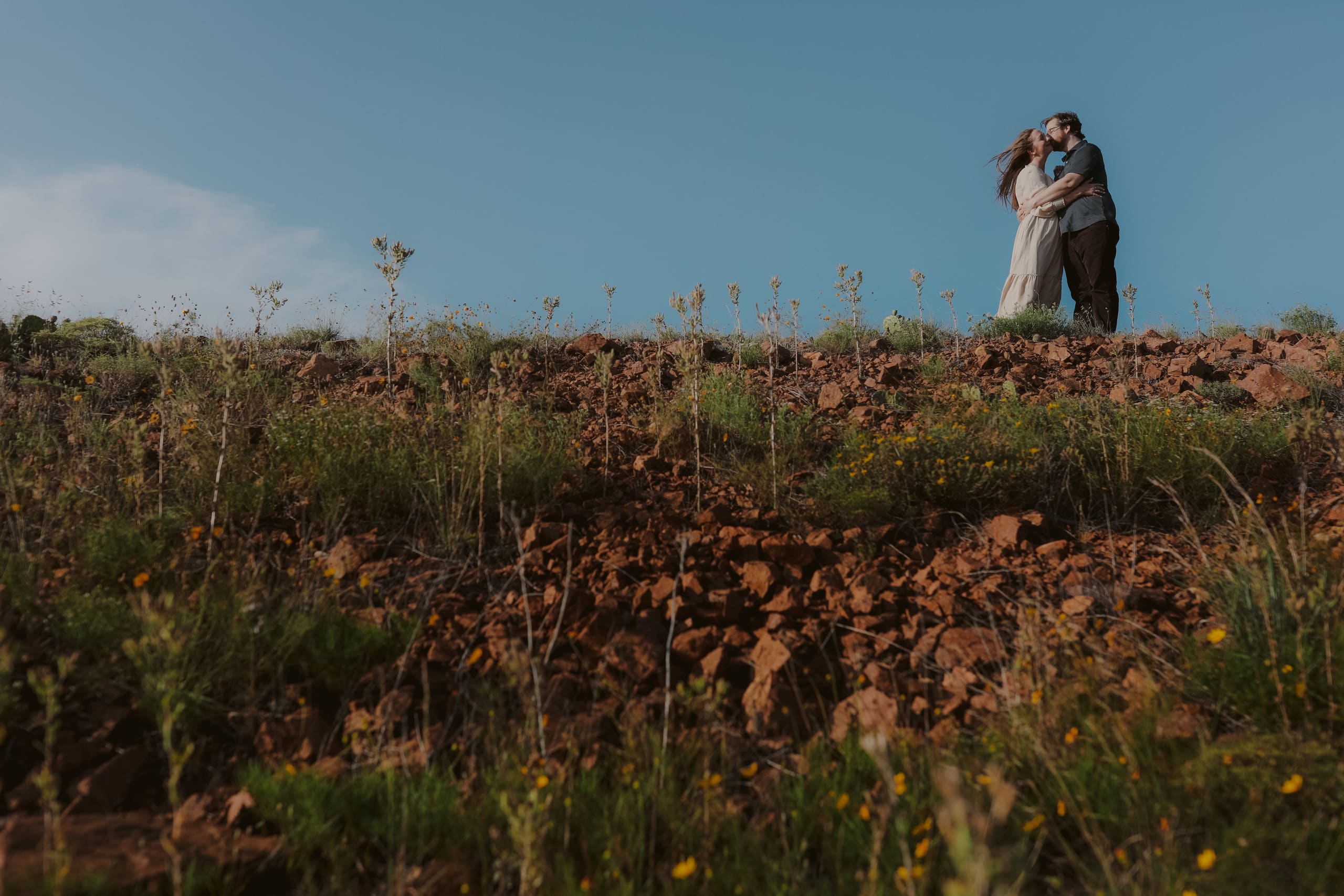 A kiss at the top of the red-rock slope, wildflowers below