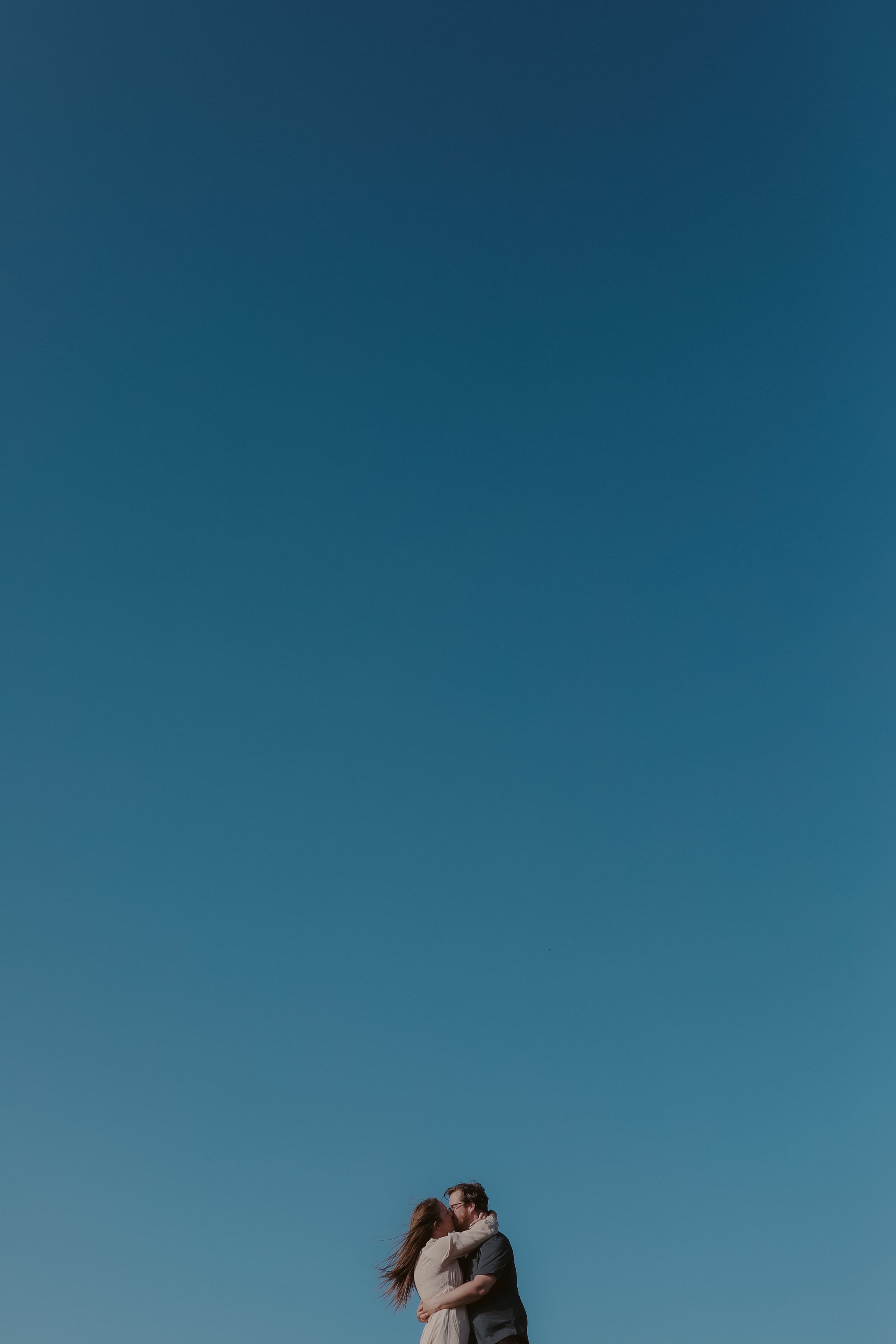 An embrace on the hilltop, small against the open sky