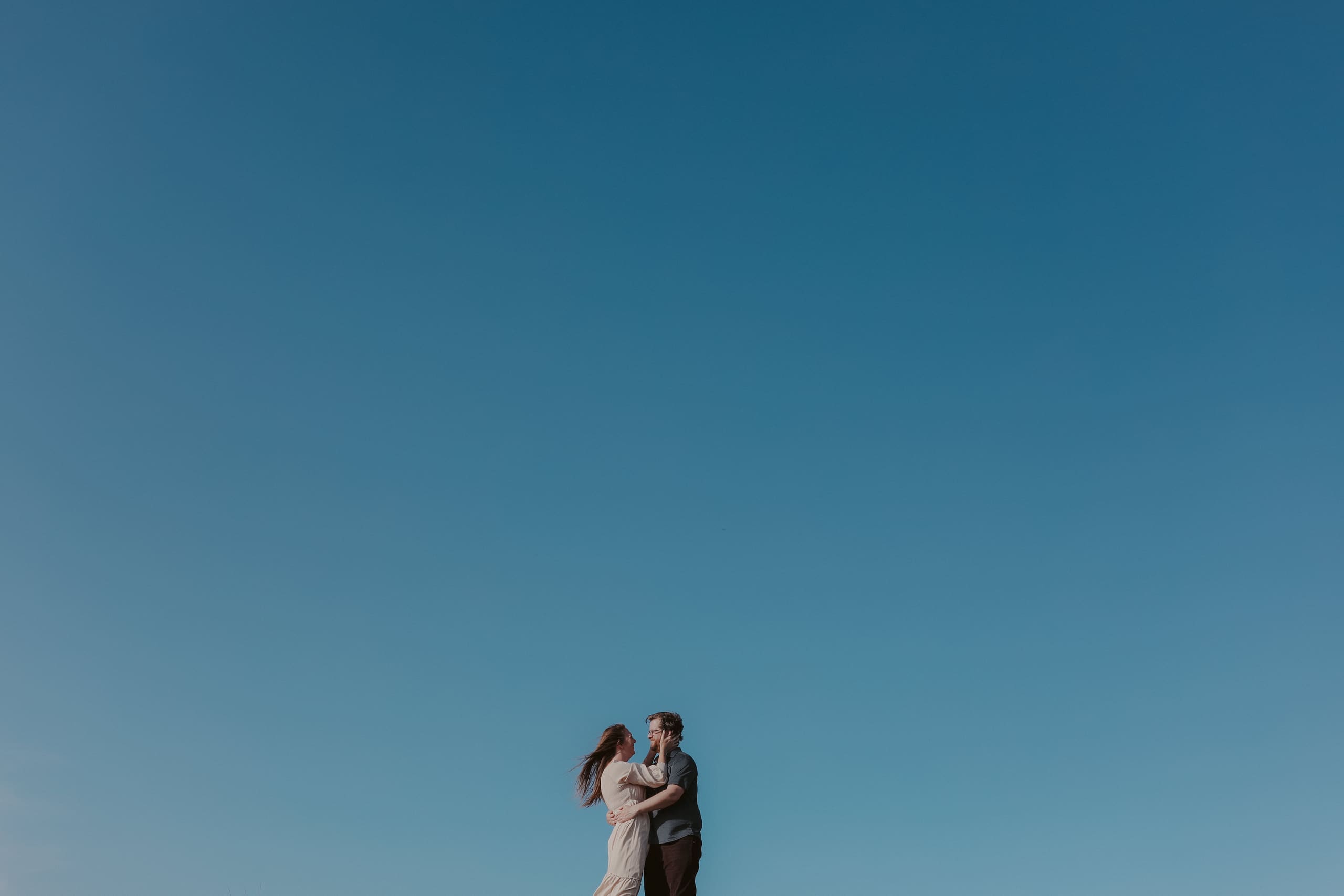 Two small figures embracing beneath an endless blue sky
