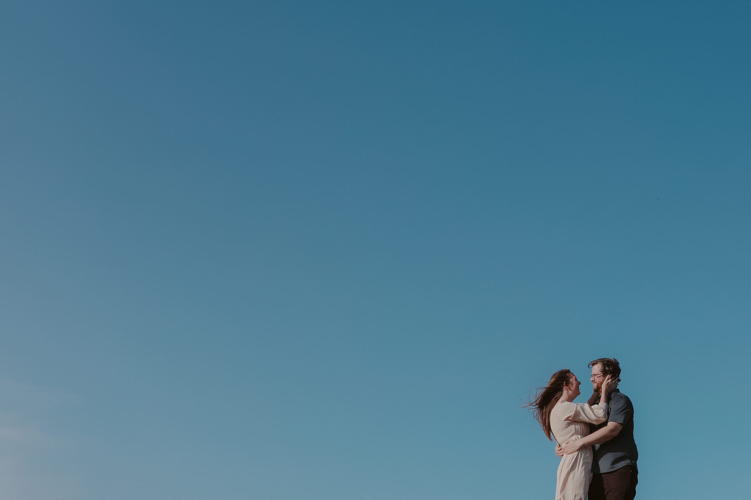 An embrace at the edge of the frame, all sky above them