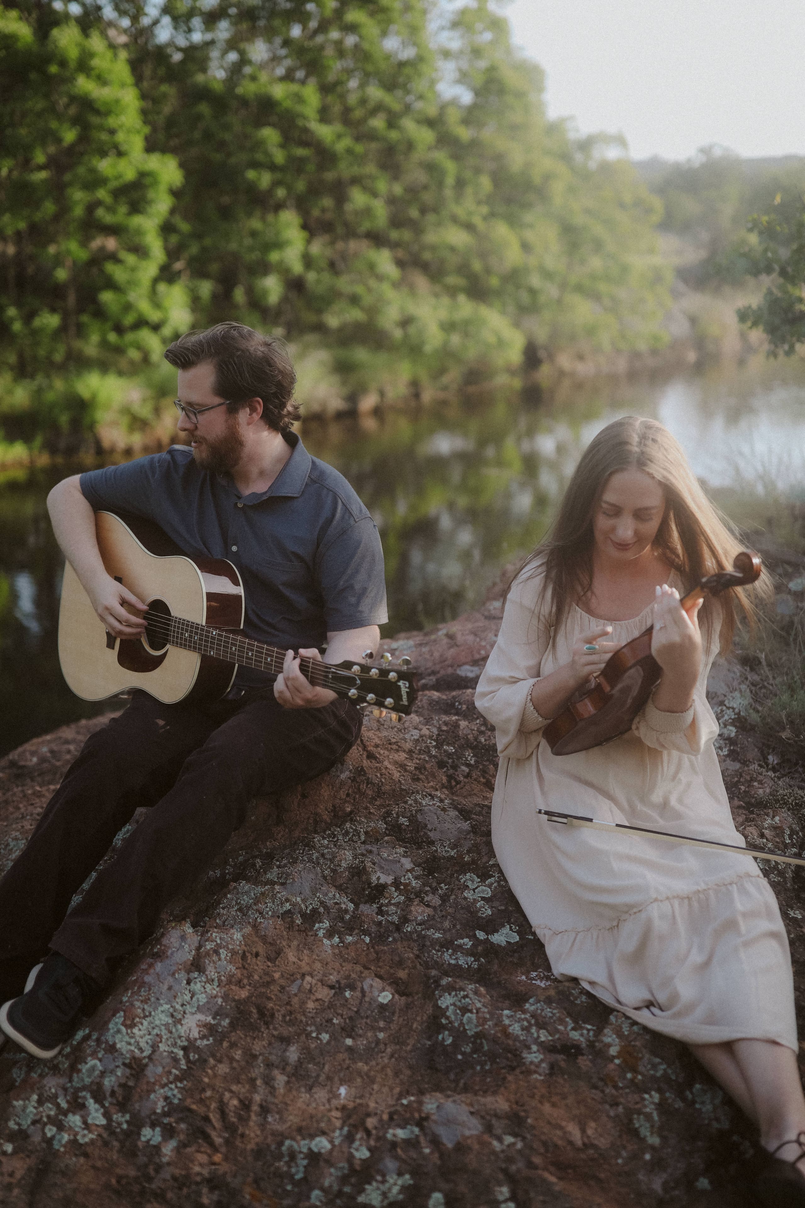 Guitar and violin on the rocks above the creek, trees glowing behind