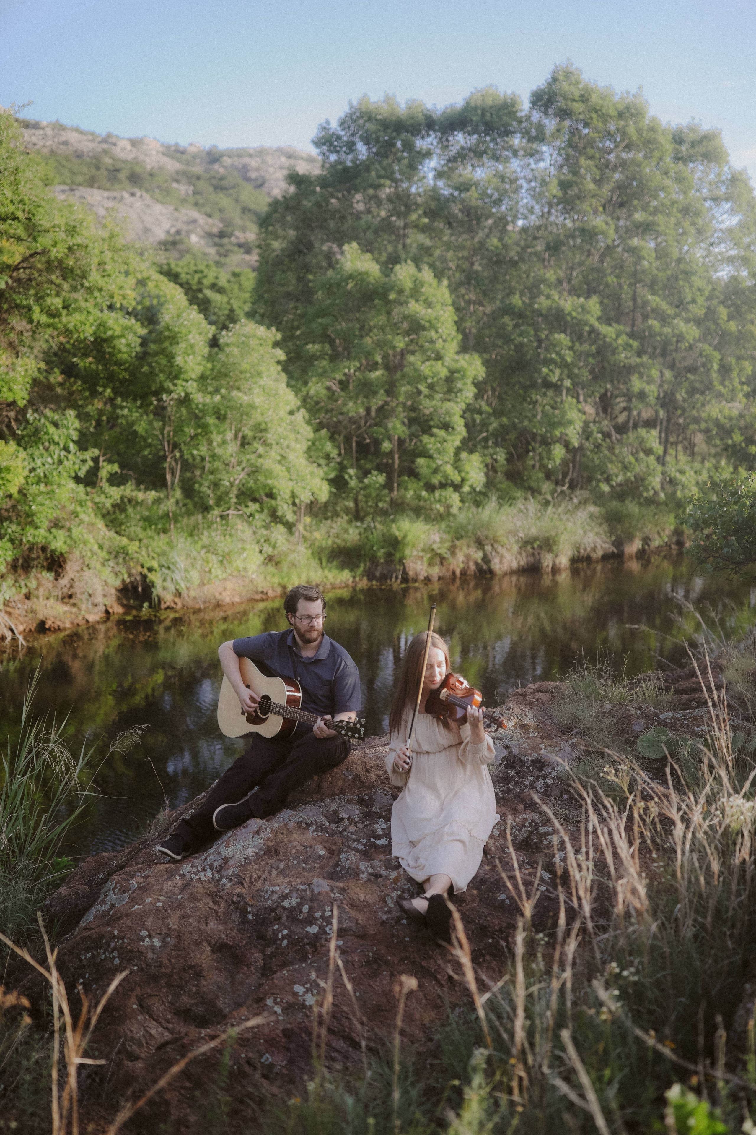 Playing guitar and violin together on a boulder above the still water