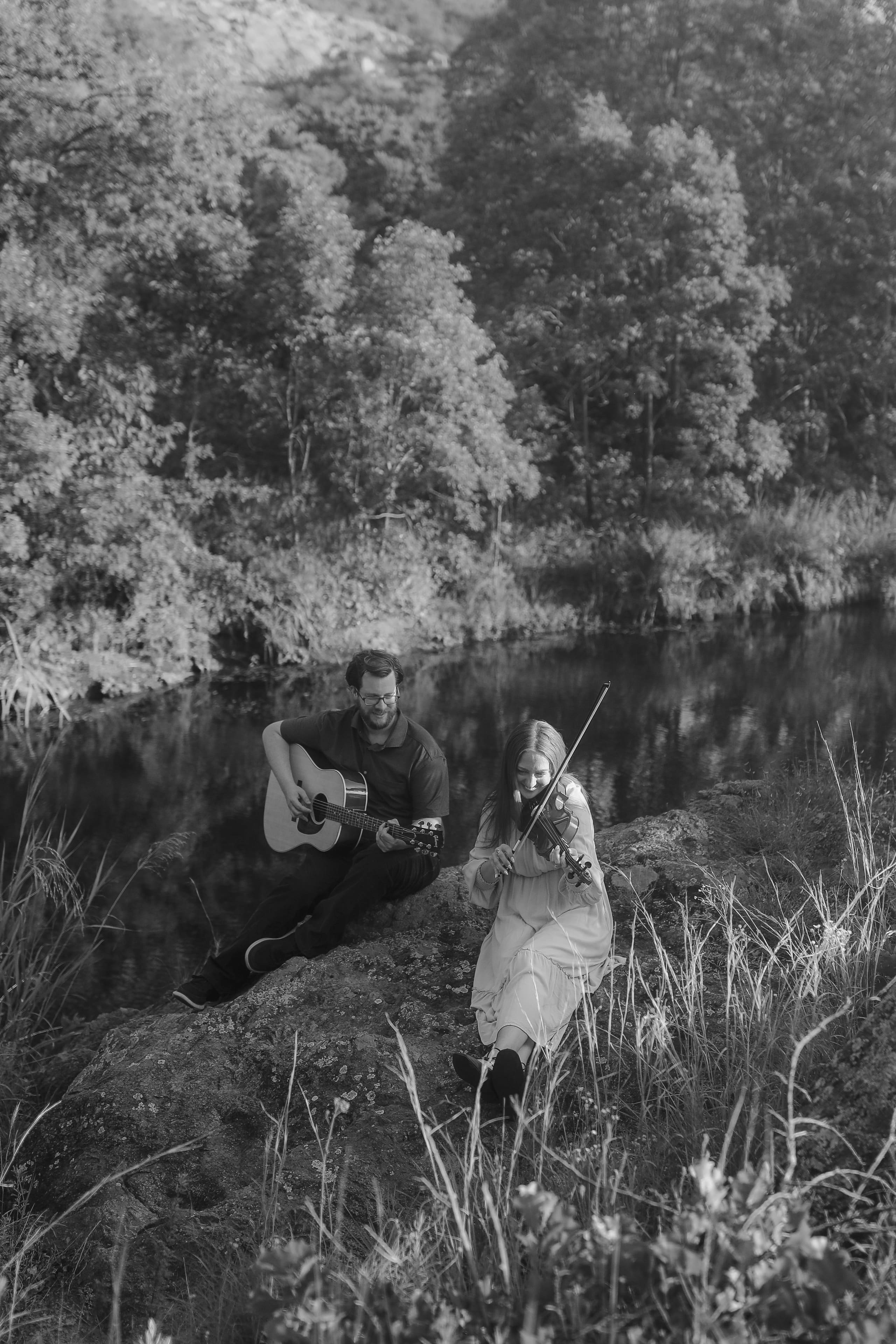 A black-and-white duet of guitar and violin at the water’s edge