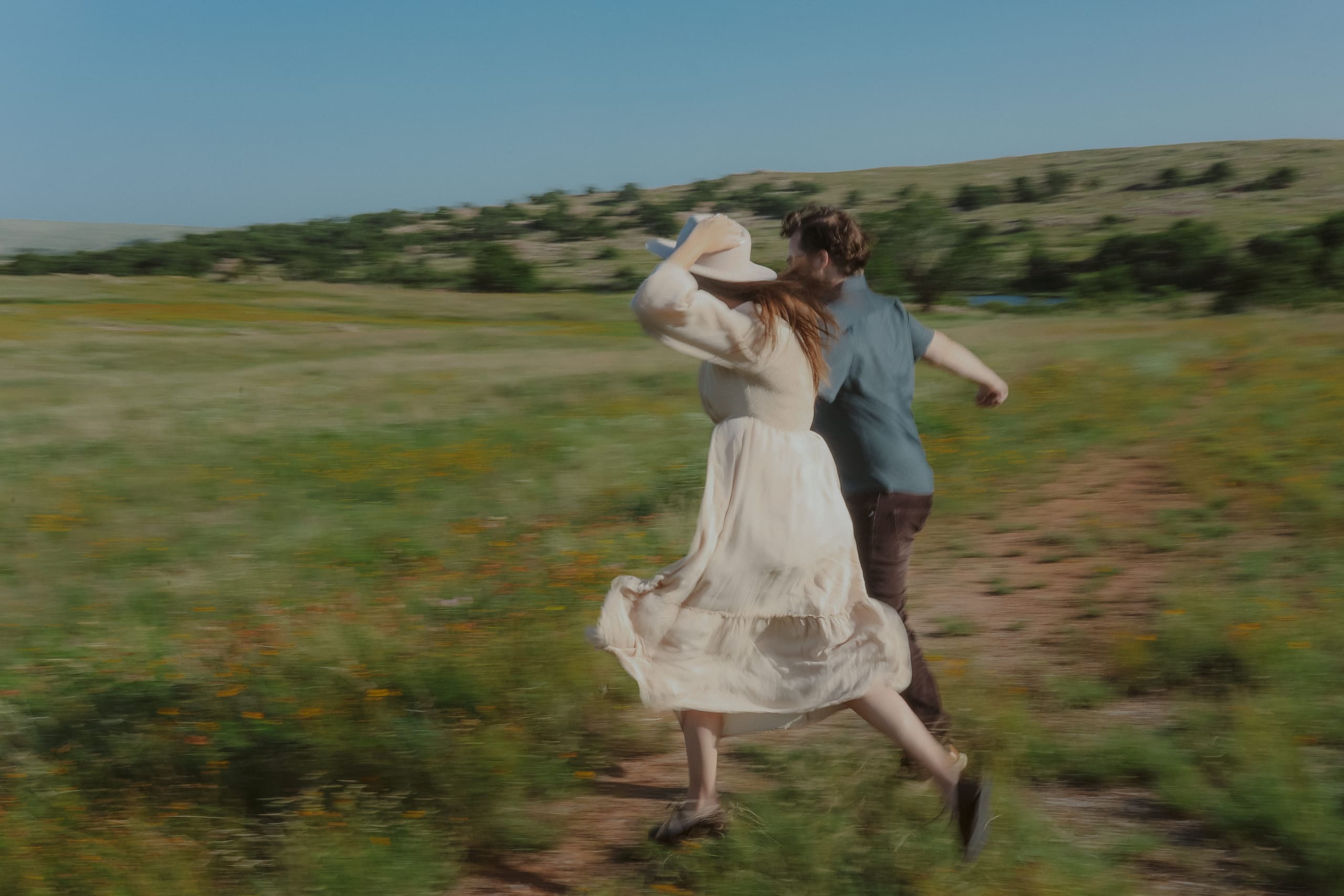 Running through the wildflowers, her hand holding her hat in the wind