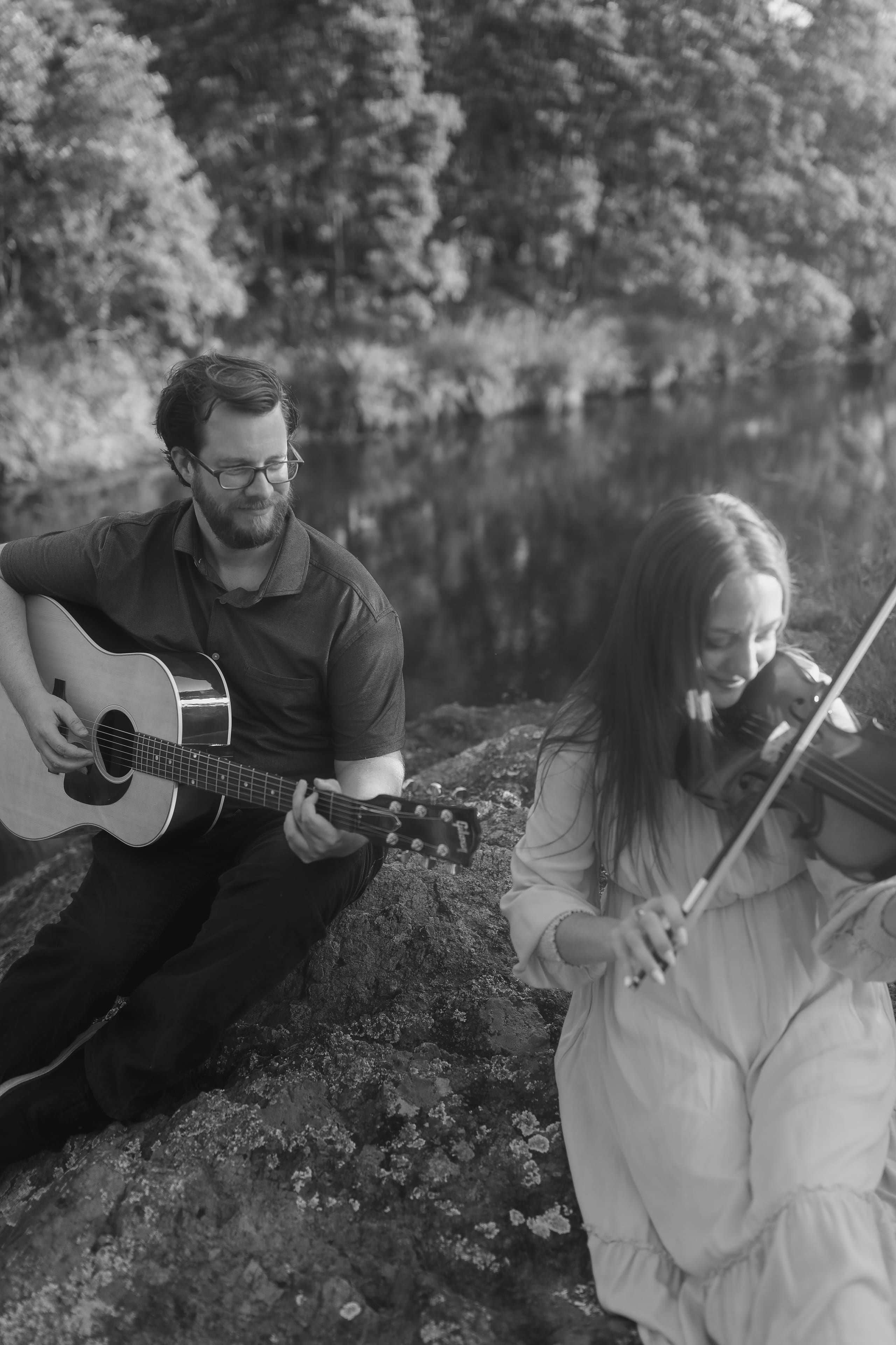 Playing guitar and violin side by side on the riverbank rocks