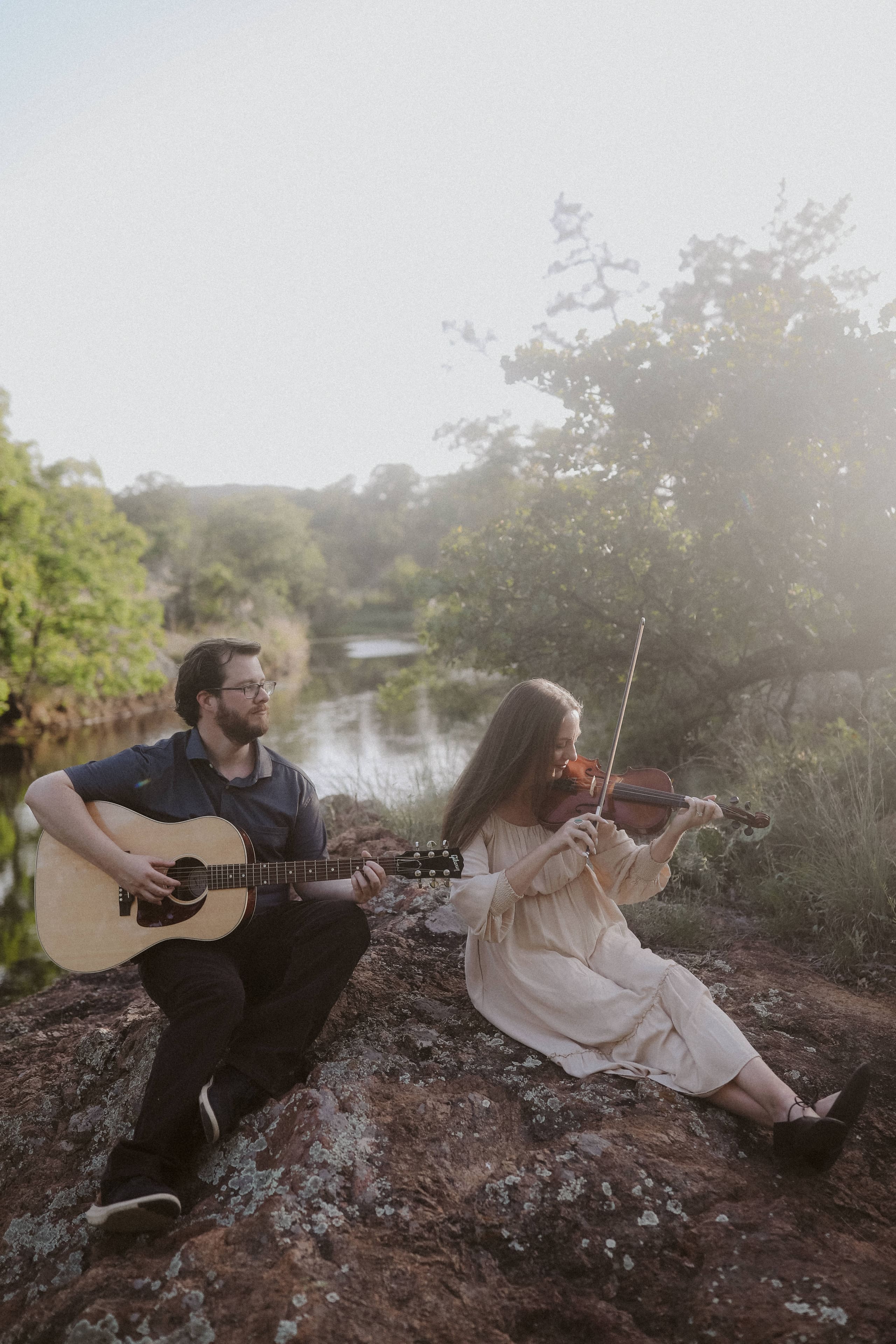 Guitar and violin on the rocks by the river, sun flaring through the trees