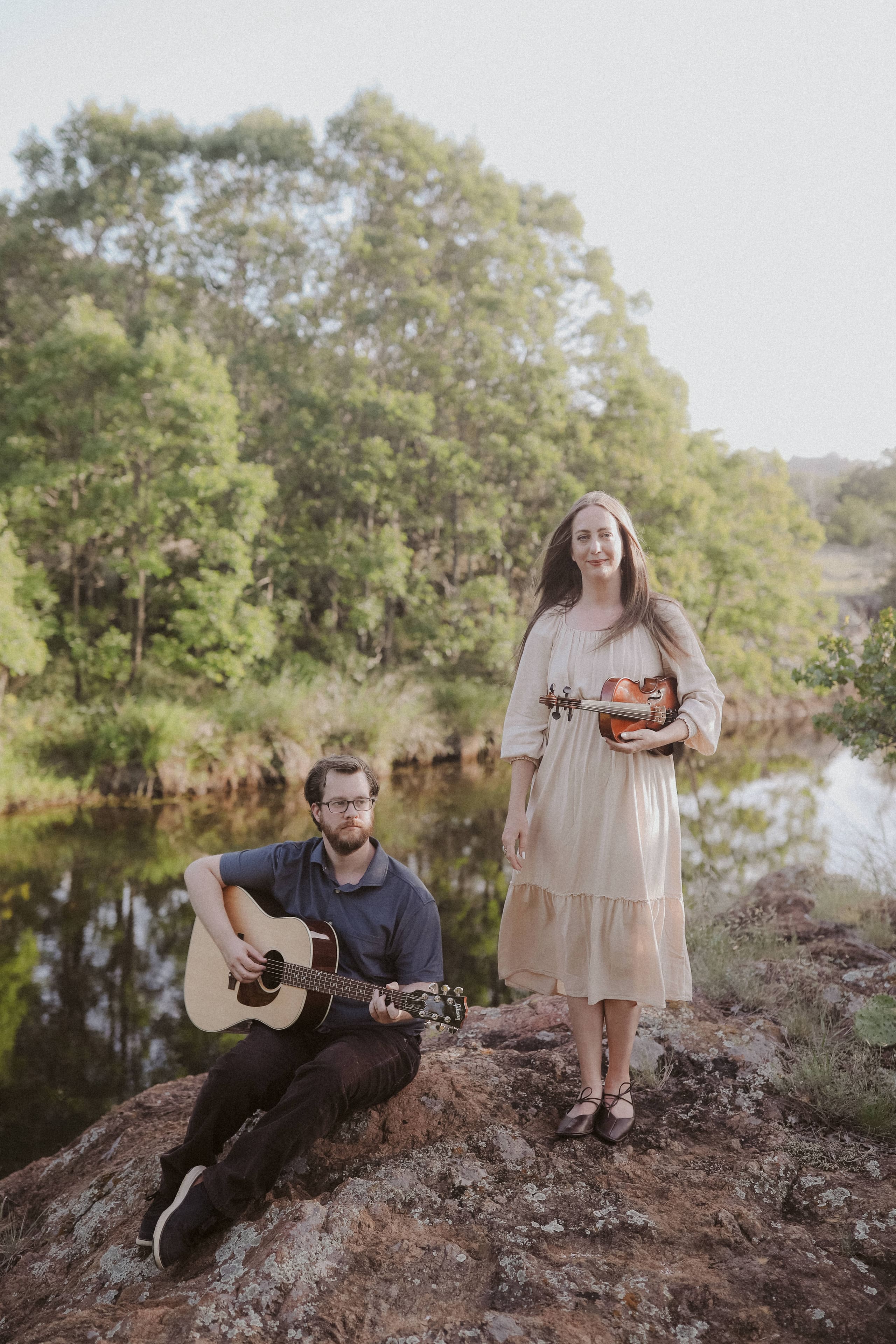 Guitar and violin on the rocks by the river, trees reflected in the still water
