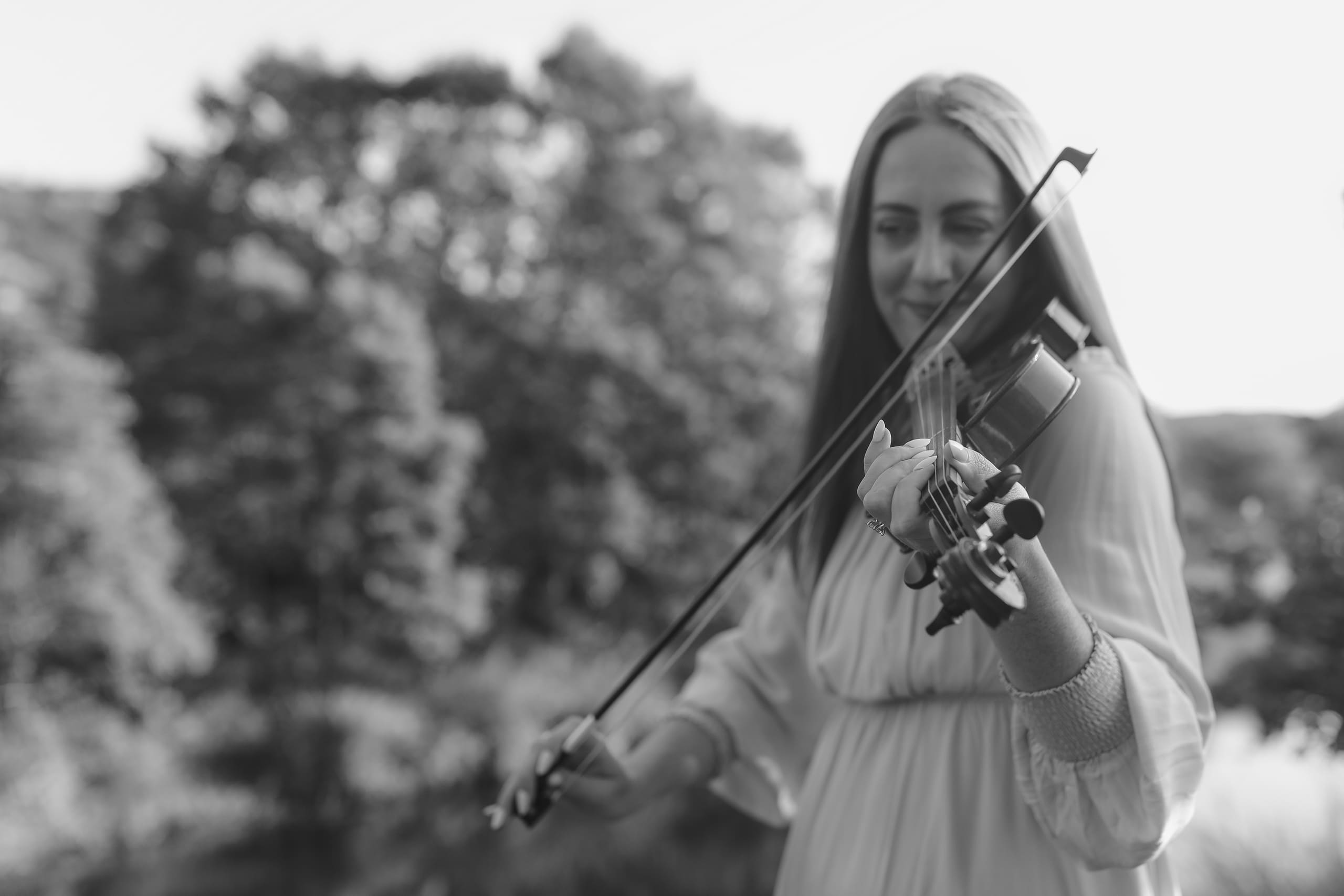 A black-and-white frame of her playing violin beneath soft summer trees