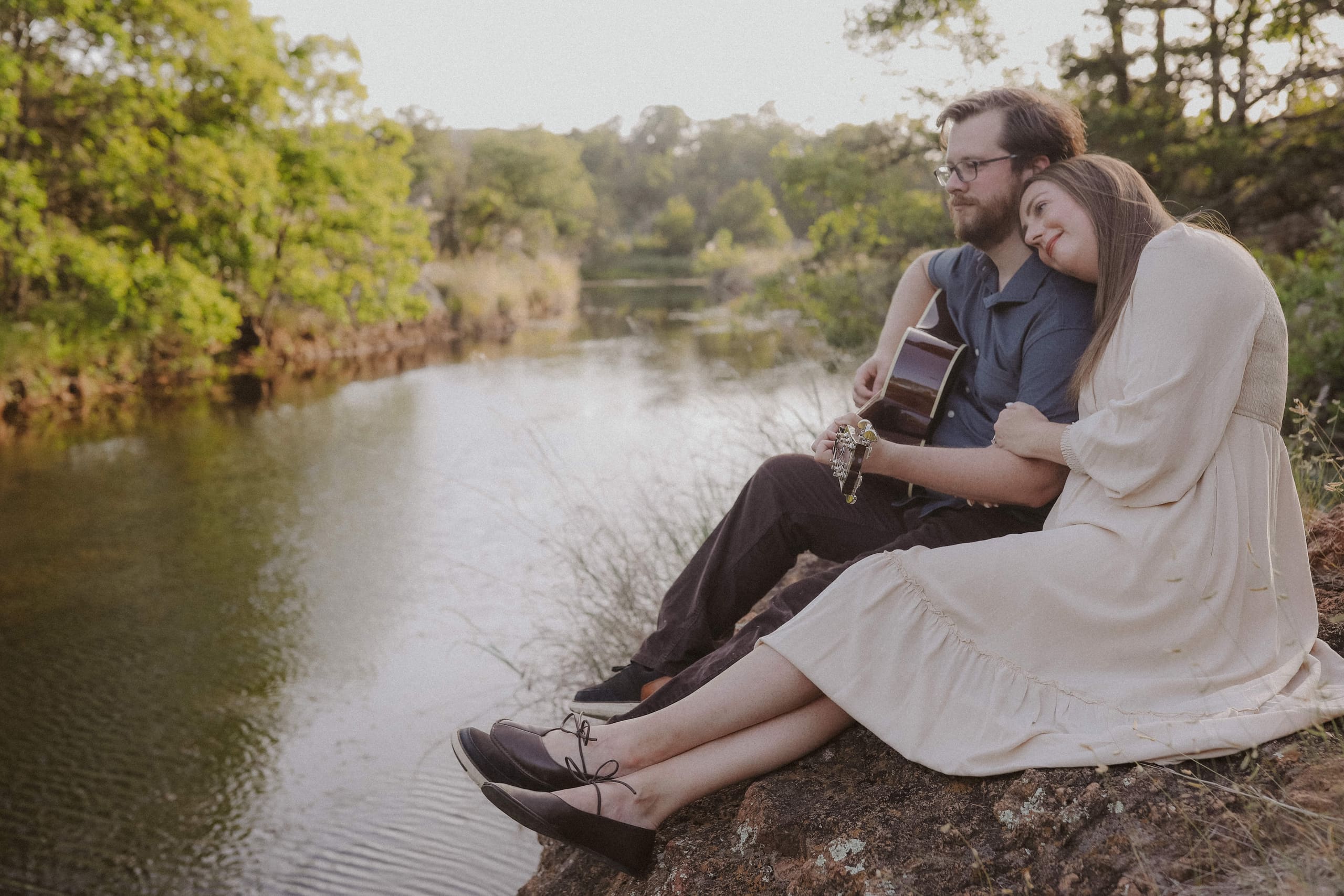 Sitting together on the riverbank, her head on his shoulder, guitar in hand