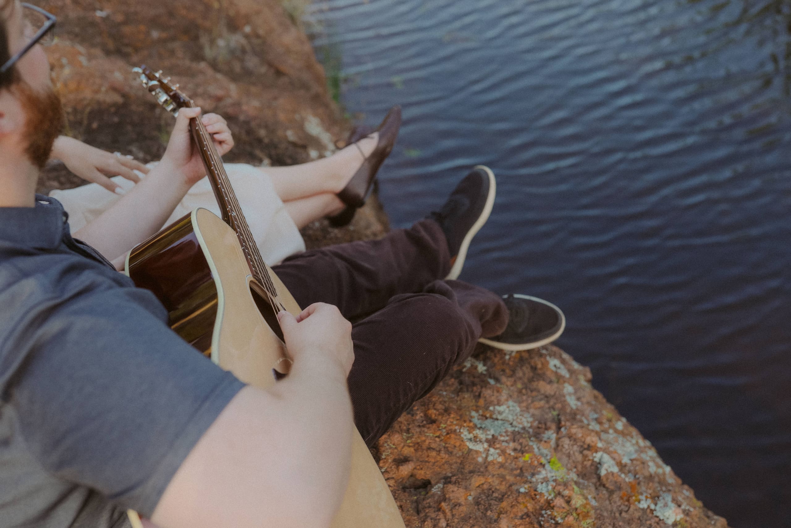 Over his shoulder — guitar in hand, shoes hovering above the water