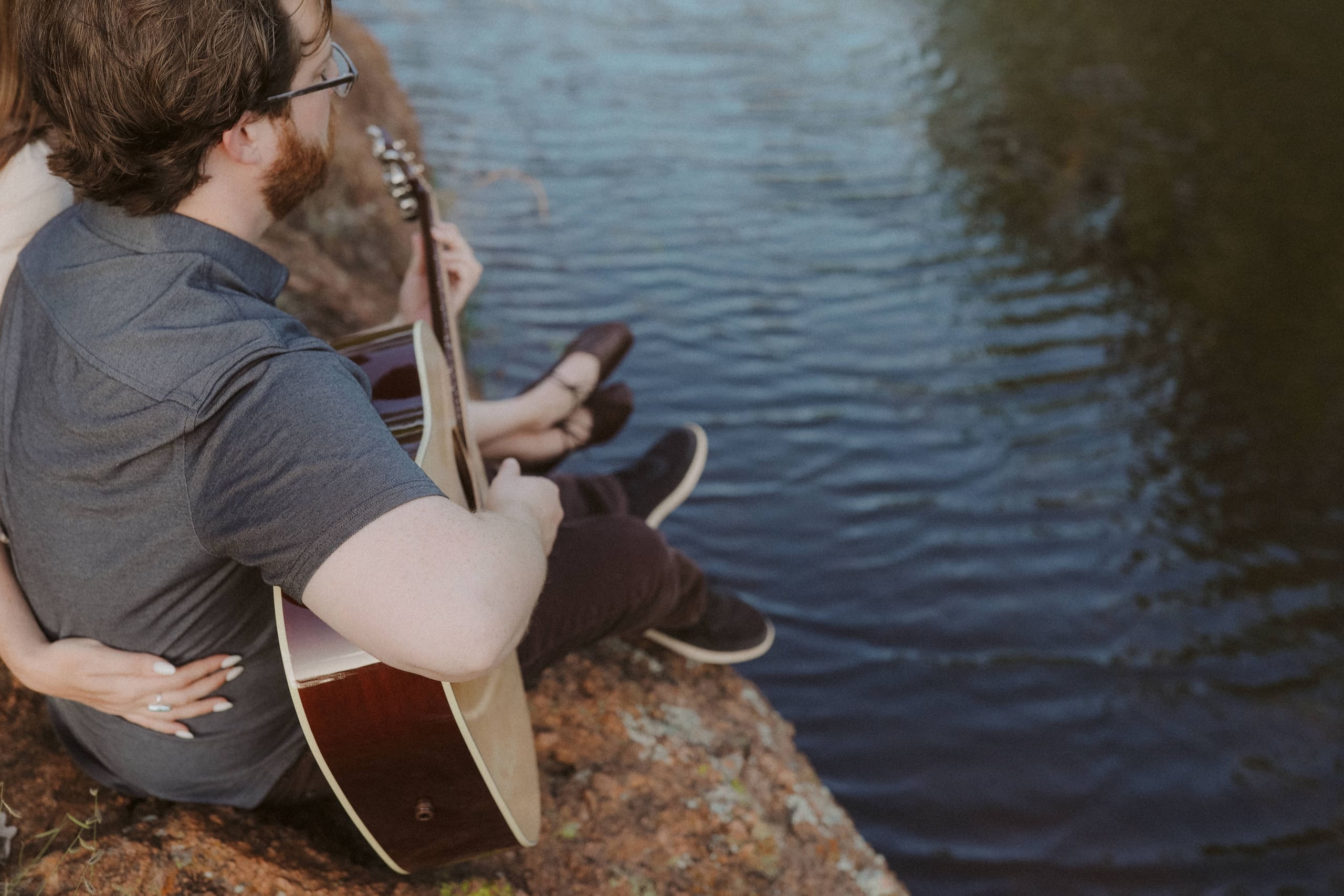 Her hand around his waist while he plays above the darkening water