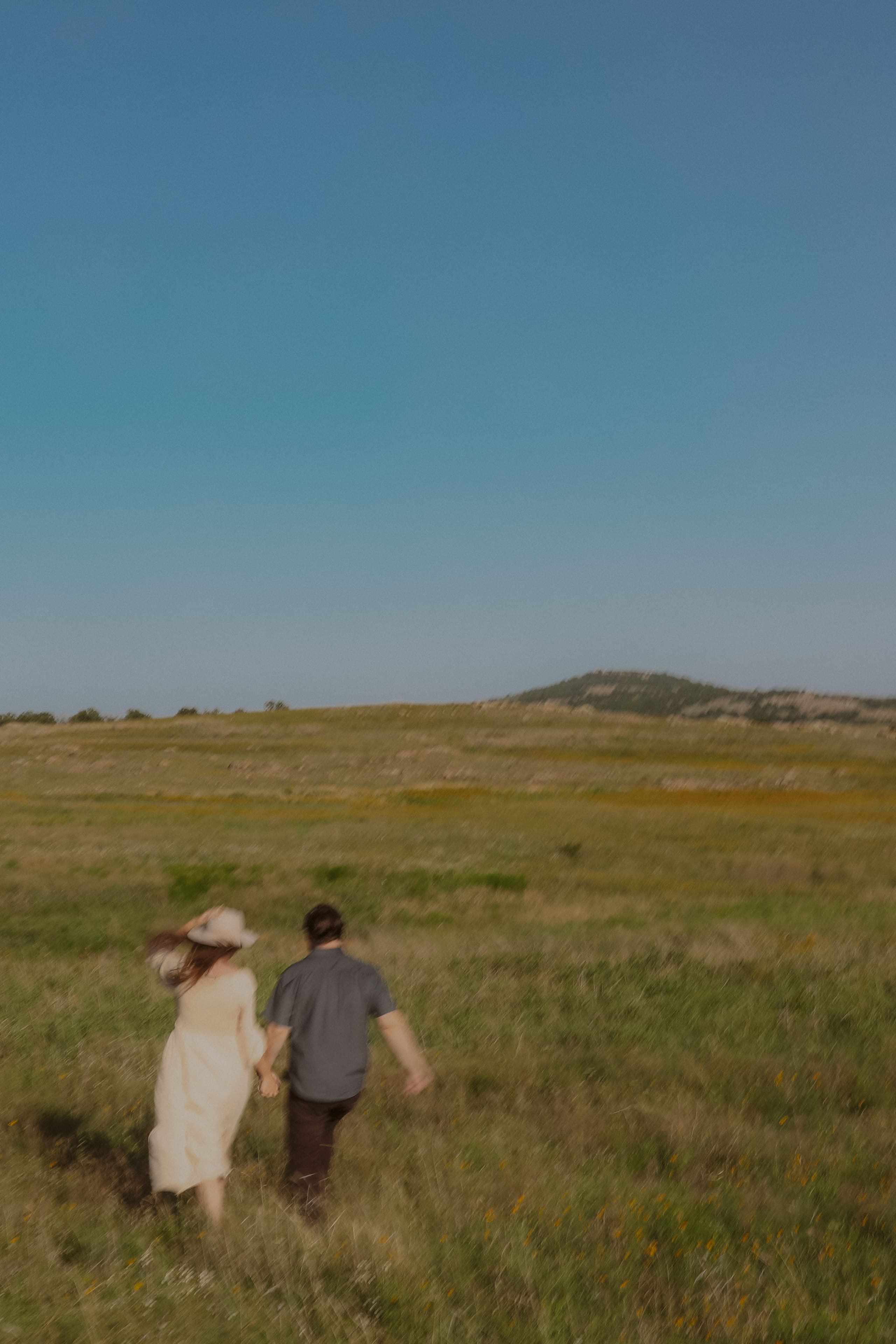 A dreamy, motion-blurred walk hand in hand through open grassland under a wide blue sky