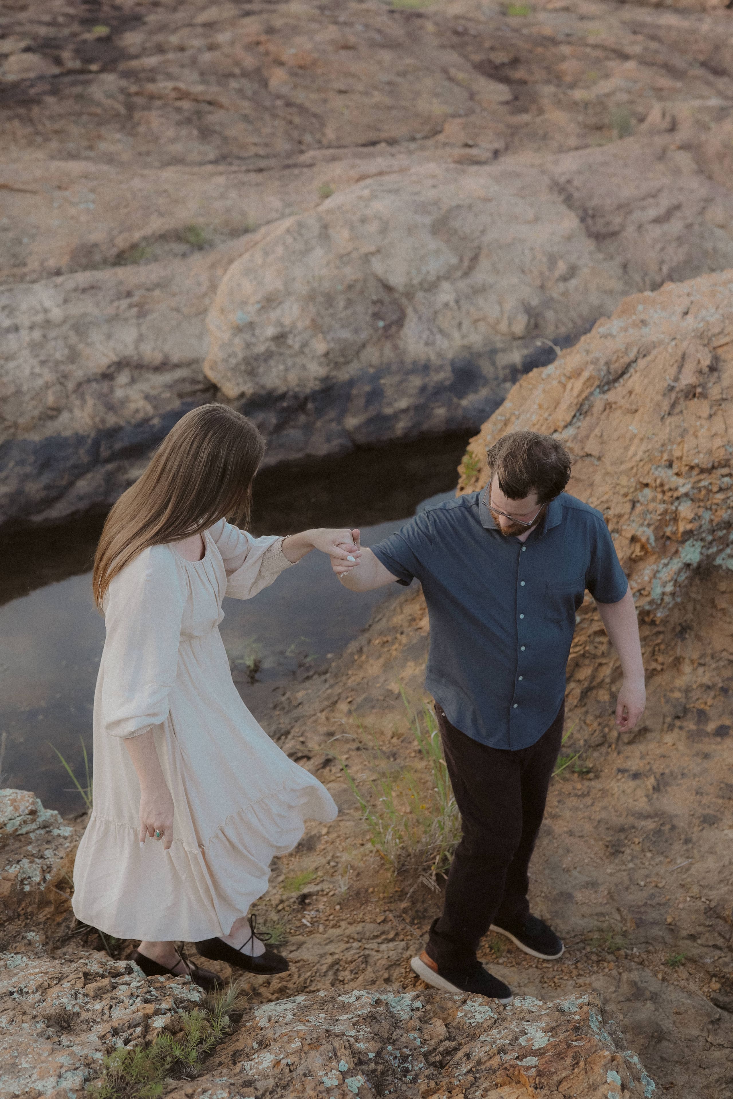 He takes her hand to guide her across the rocks