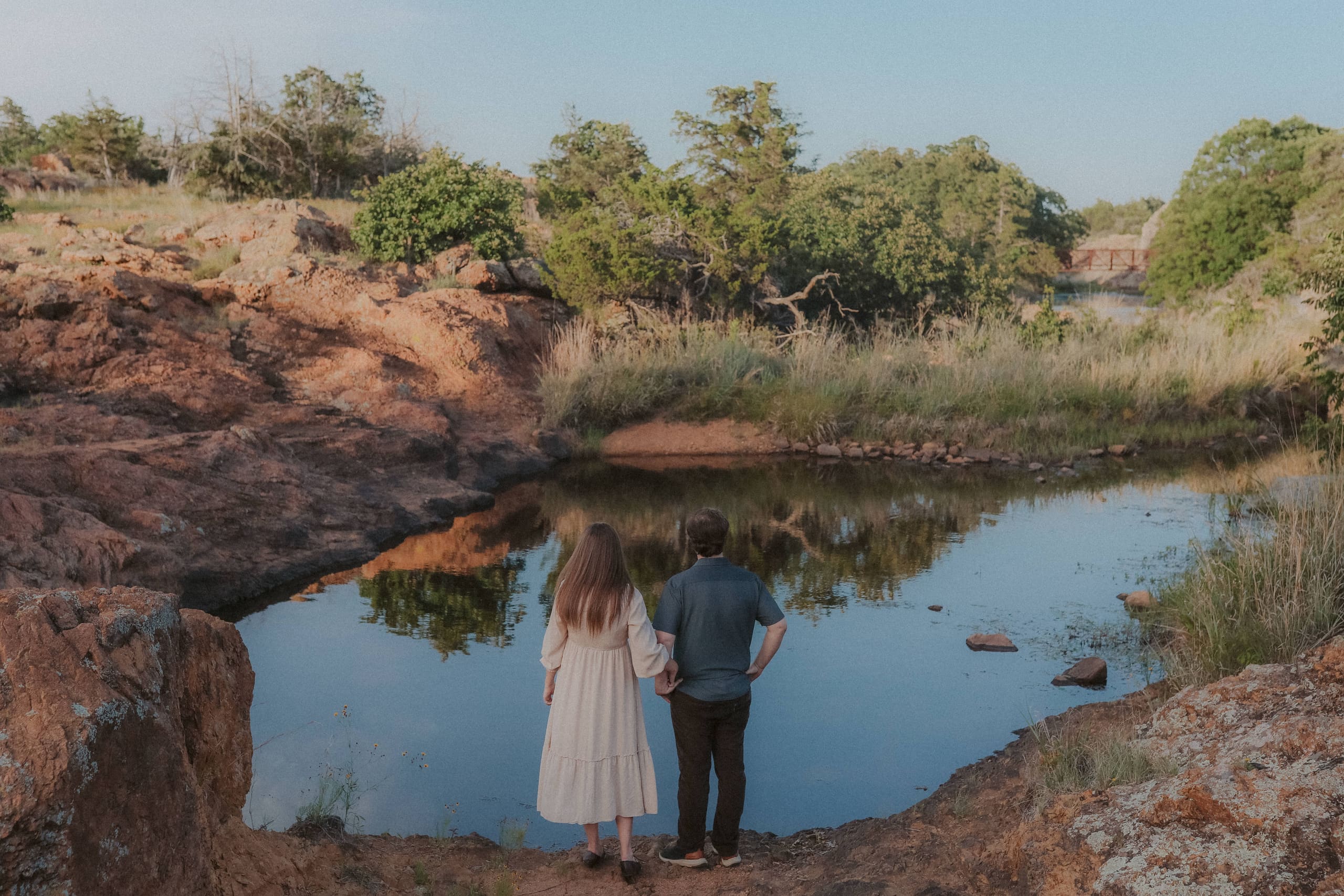 Hand in hand at the water’s edge, trees and sky mirrored in the pool