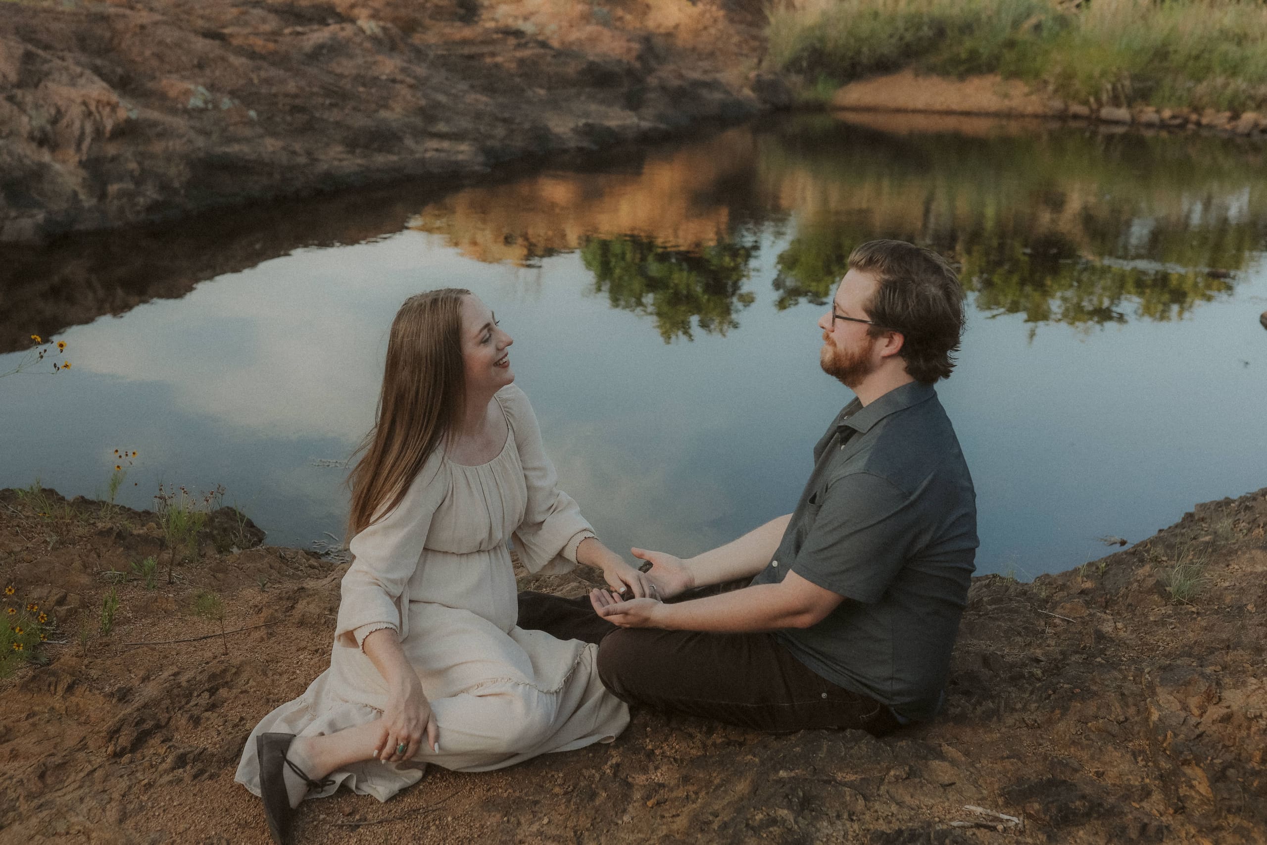 Sitting together at the pond’s edge, hands joined, trees mirrored in still water