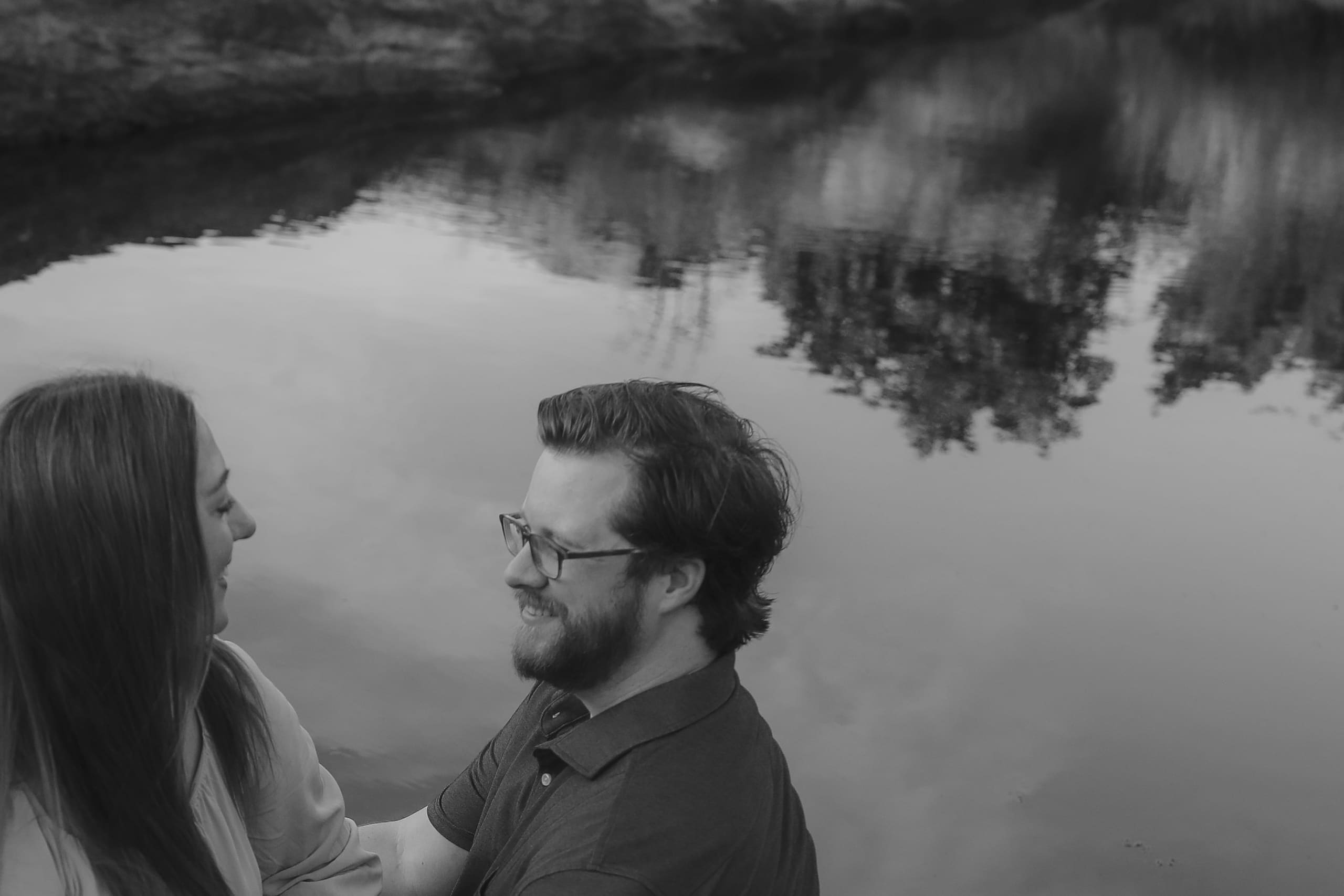 A shared smile at the water’s edge, trees reflected in black and white