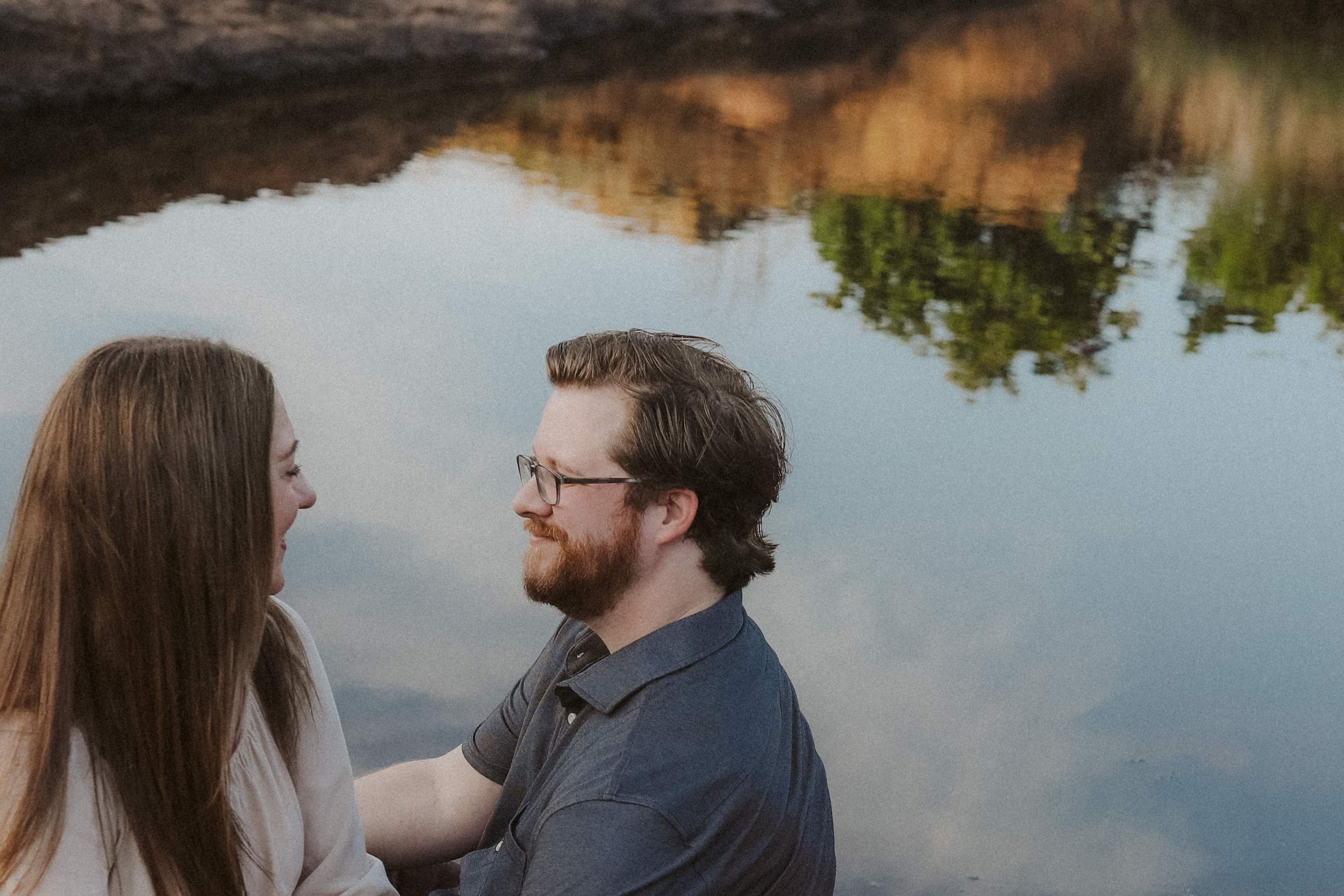 Face to face beside still water, evening color reflected behind them