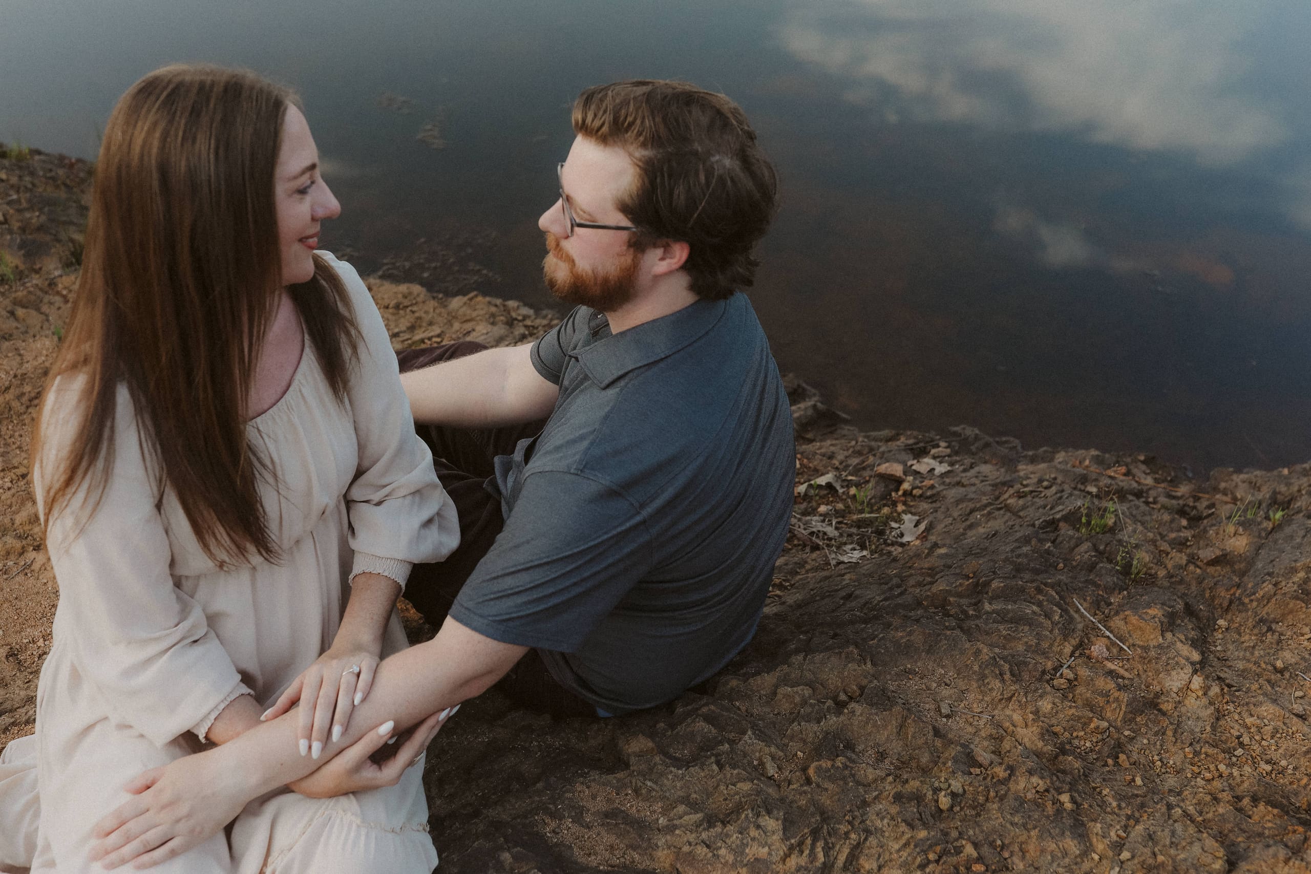 Seated on the rocky shore, her hand resting gently on his arm