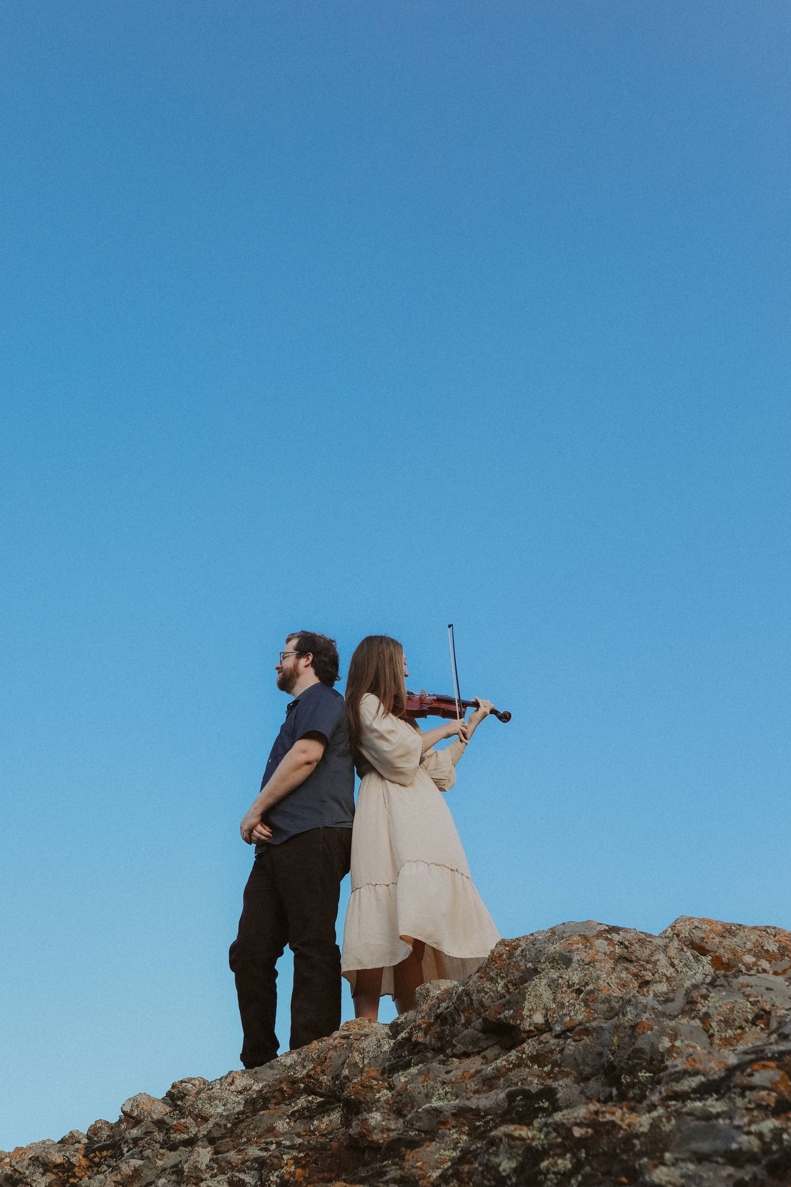 Back to back on a granite outcrop, violin raised to the blue sky