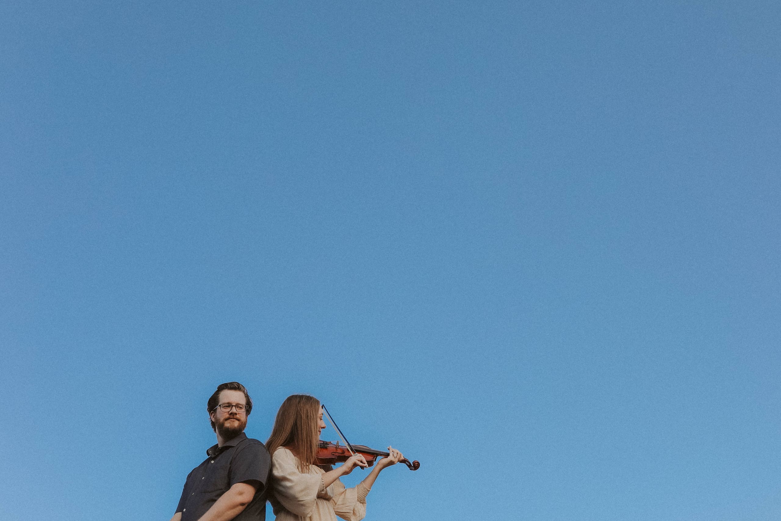 Two figures small against a wide blue sky, violin in hand