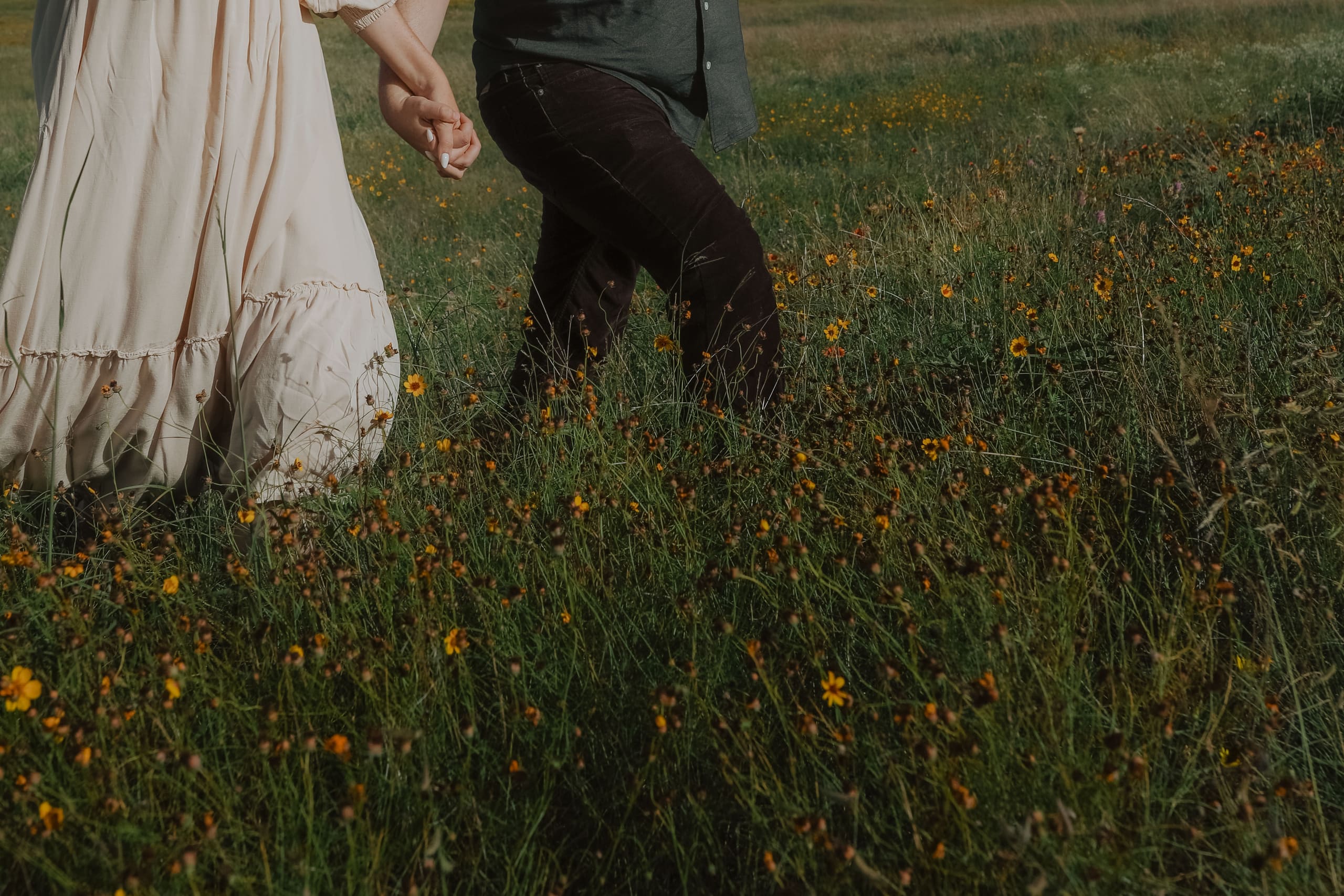 Hands clasped walking through yellow wildflowers