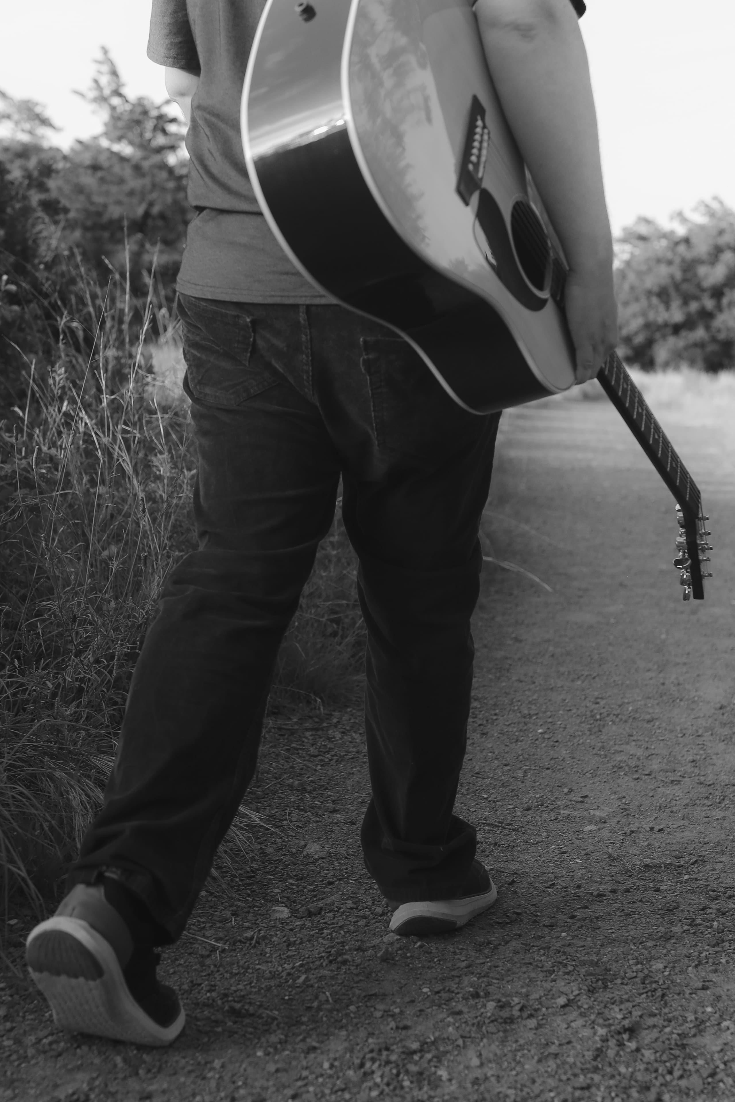 Guitar slung over his shoulder on the path, tall grasses at the edge
