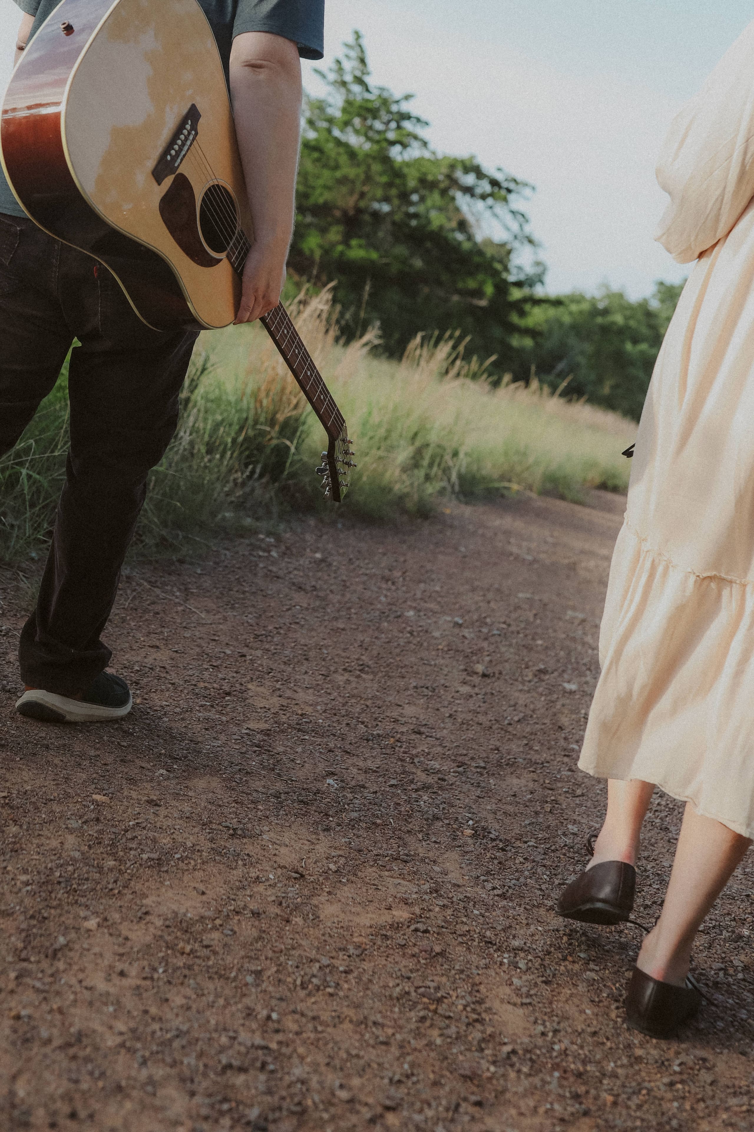 Guitar in hand on the dirt path, her dress catching the light