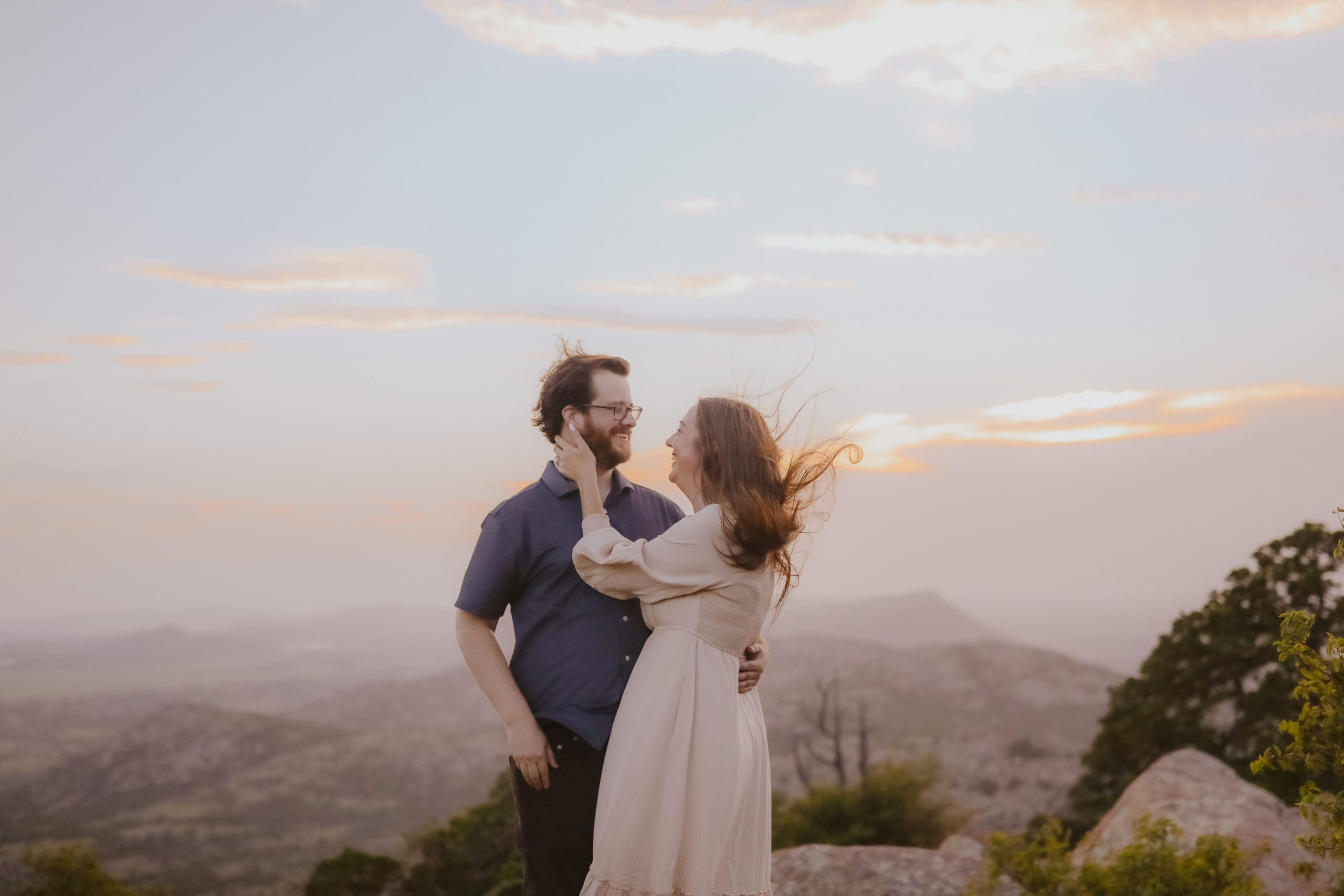 An embrace on the summit at sunset, hills hazy below