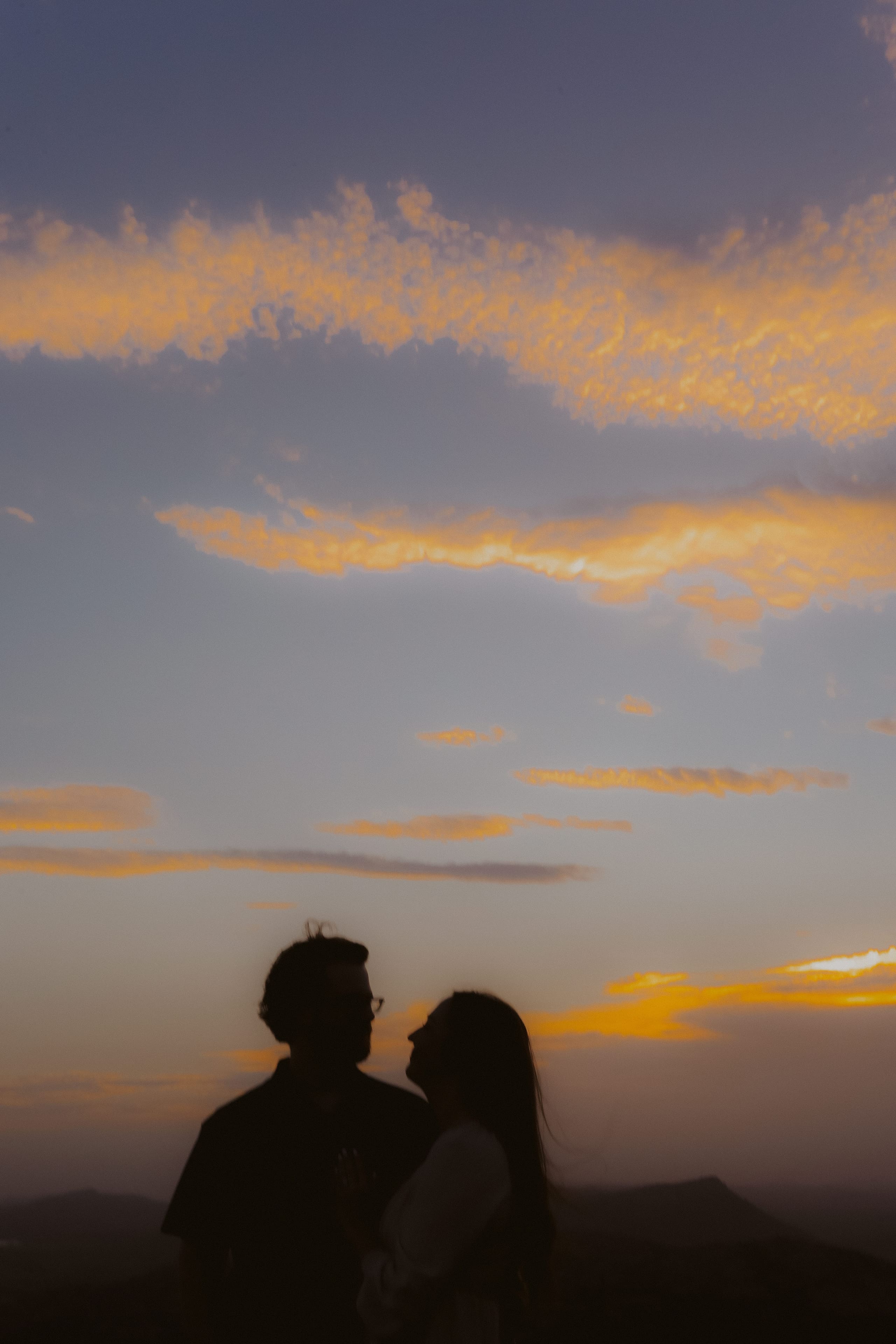 Two silhouettes against a sky streaked with sunset clouds