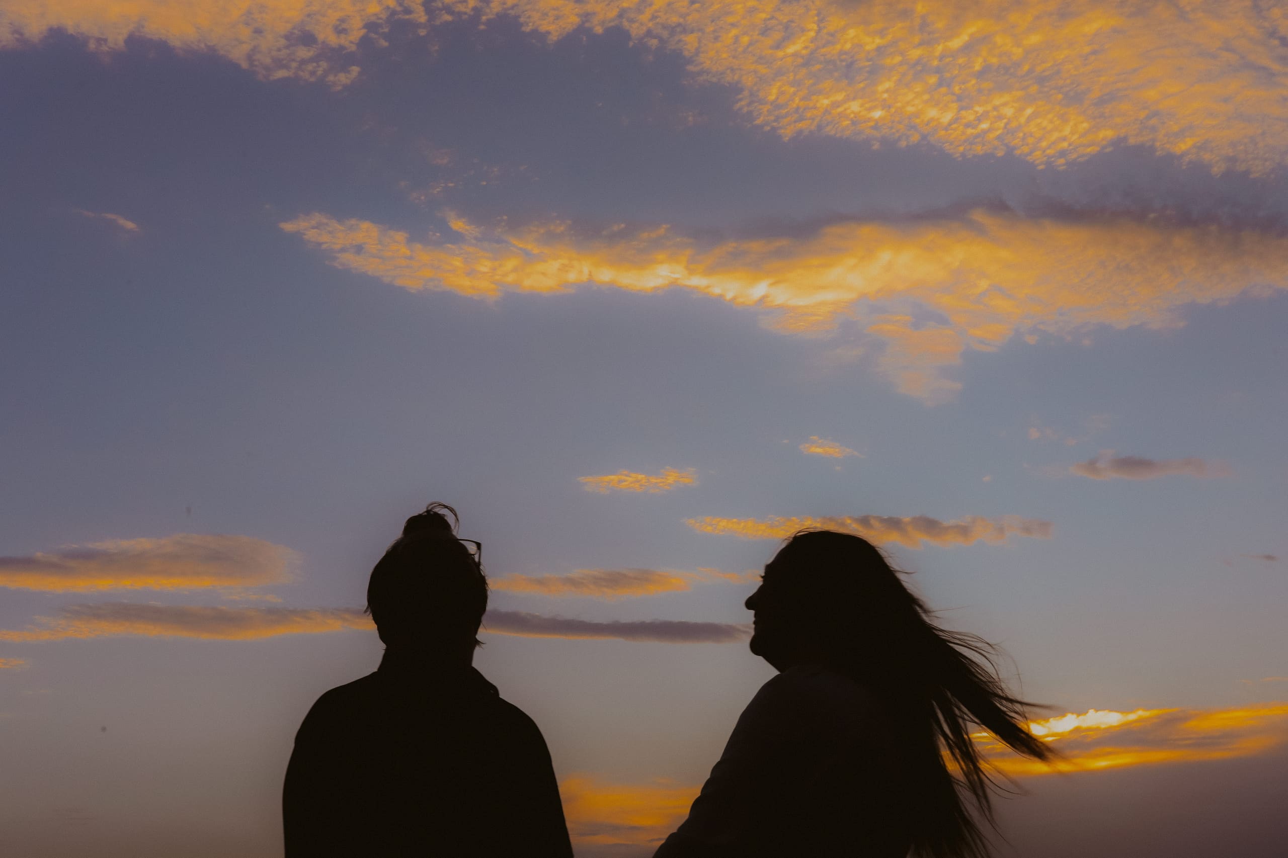 Two silhouettes turned toward each other beneath golden evening clouds