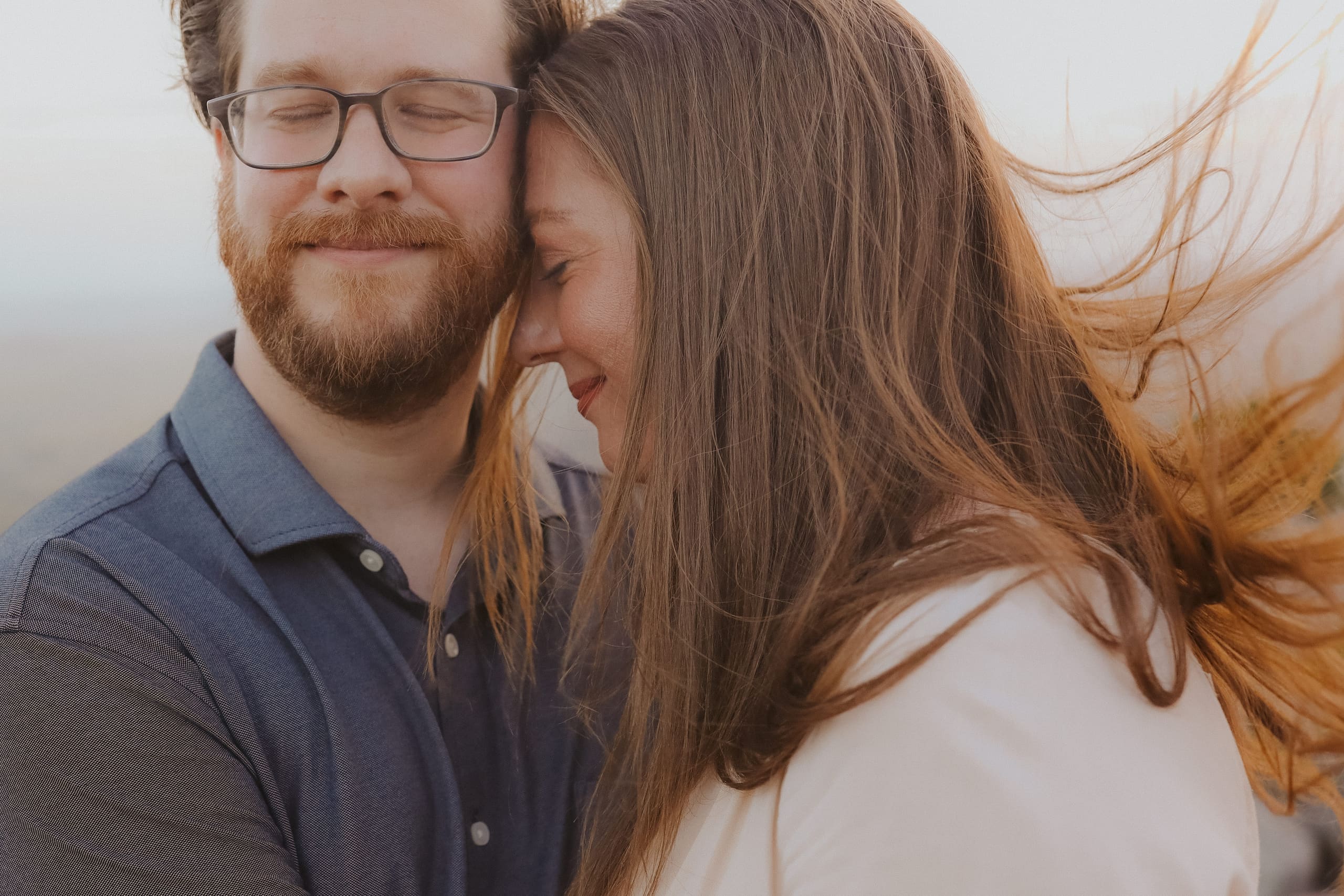 Foreheads together in soft light, her hair glowing in the breeze