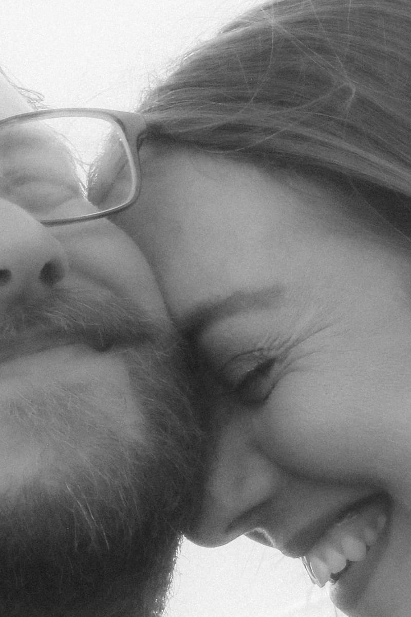 A black-and-white close-up — foreheads together, laughing into the light