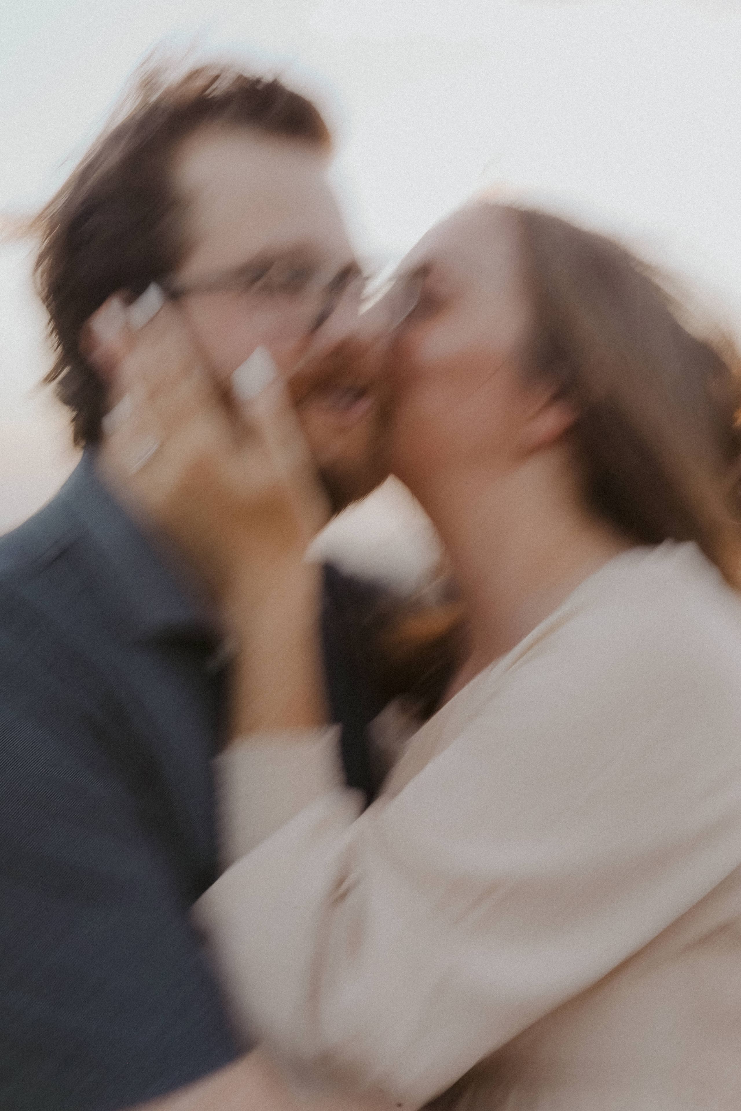 A blurred close kiss, her hand cradling his cheek in soft light