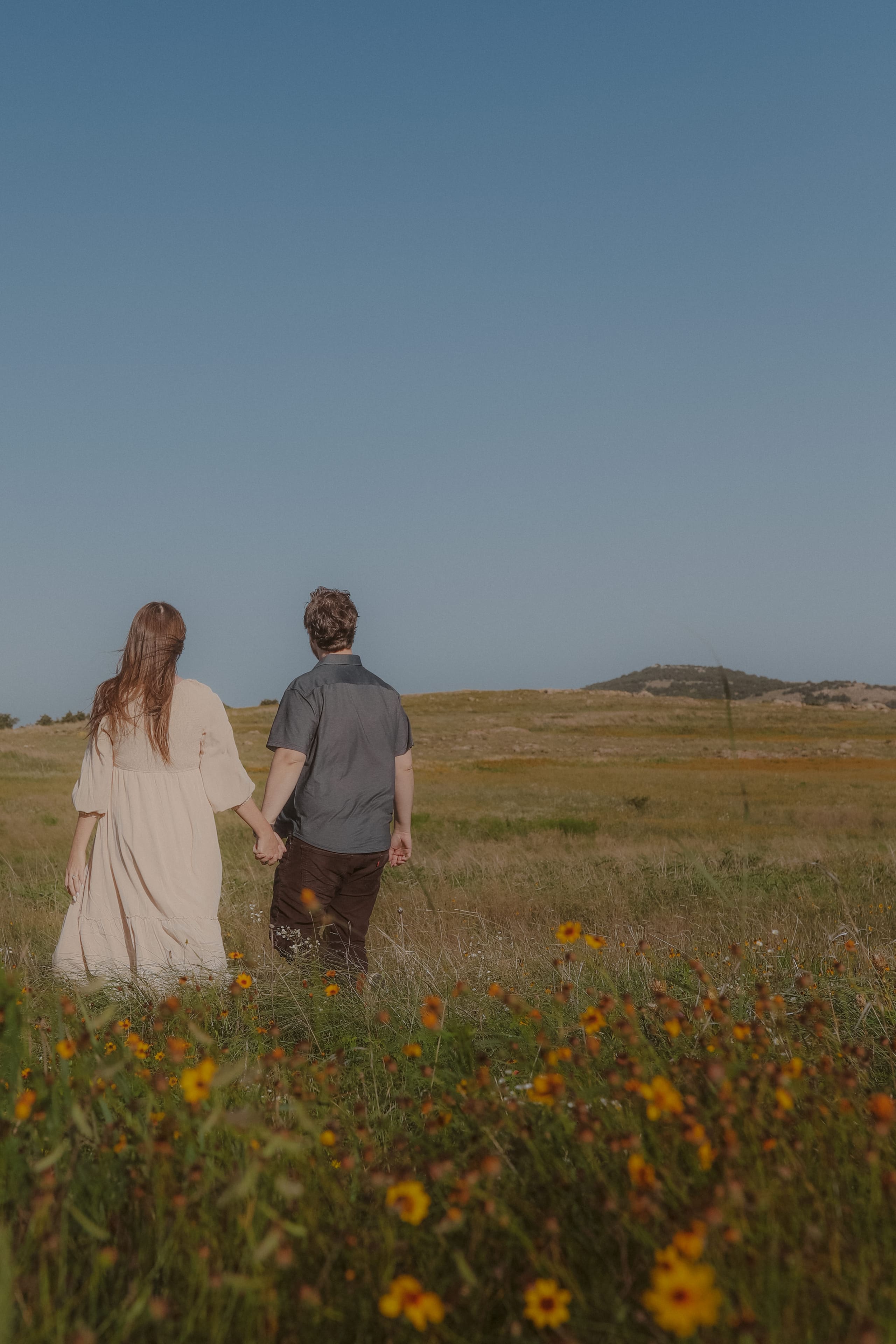 Hand in hand among the wildflowers, looking out toward the distant hills