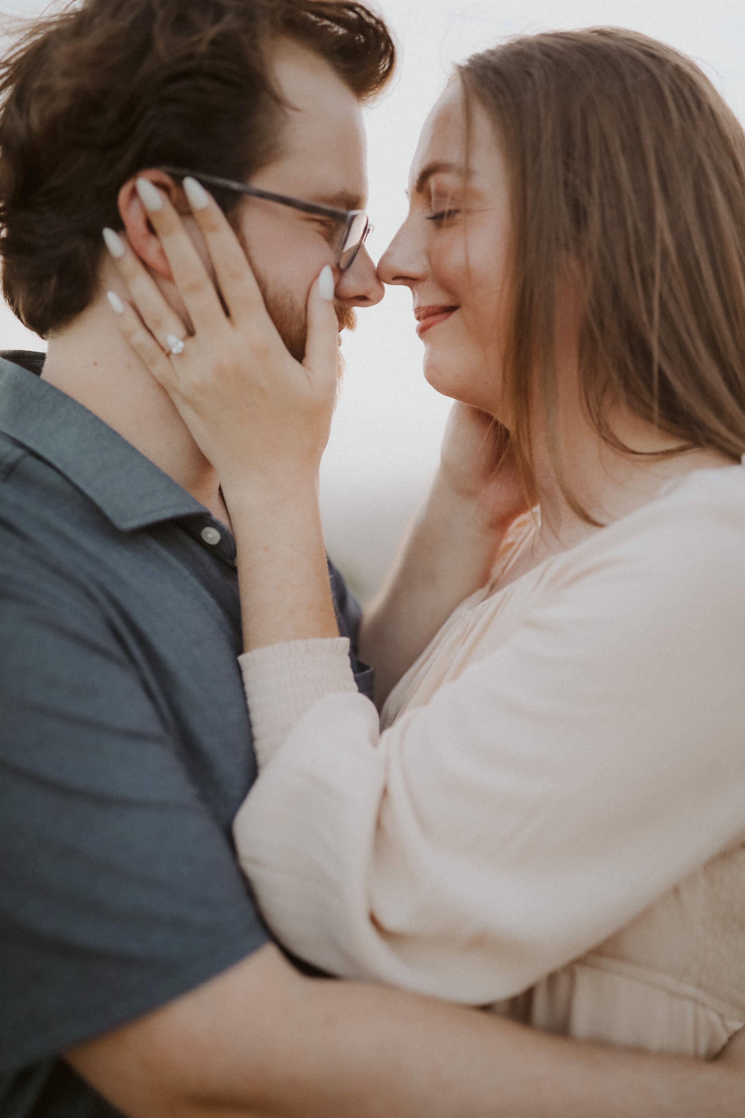 Almost a kiss — her hands framing his face at golden hour