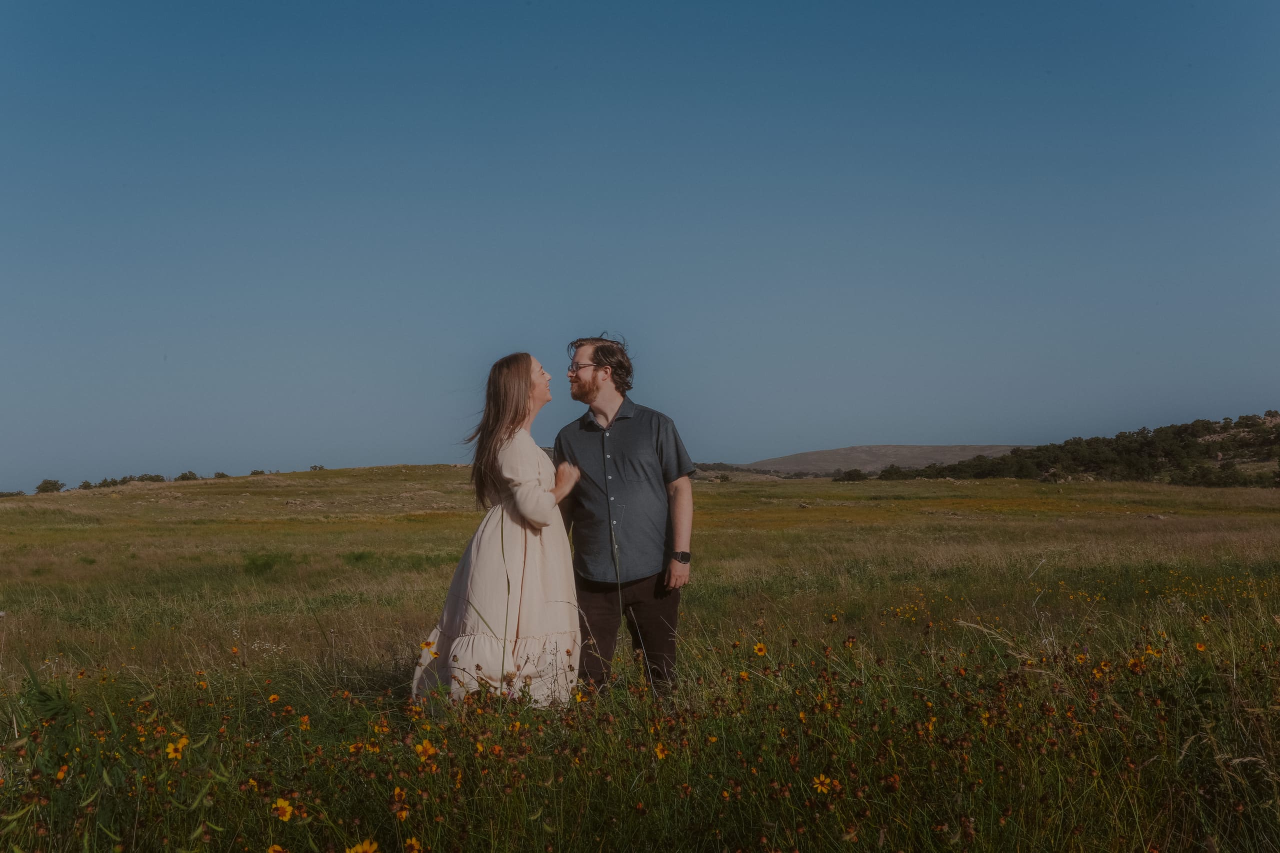 Standing close in the wildflower field, smiling at each other