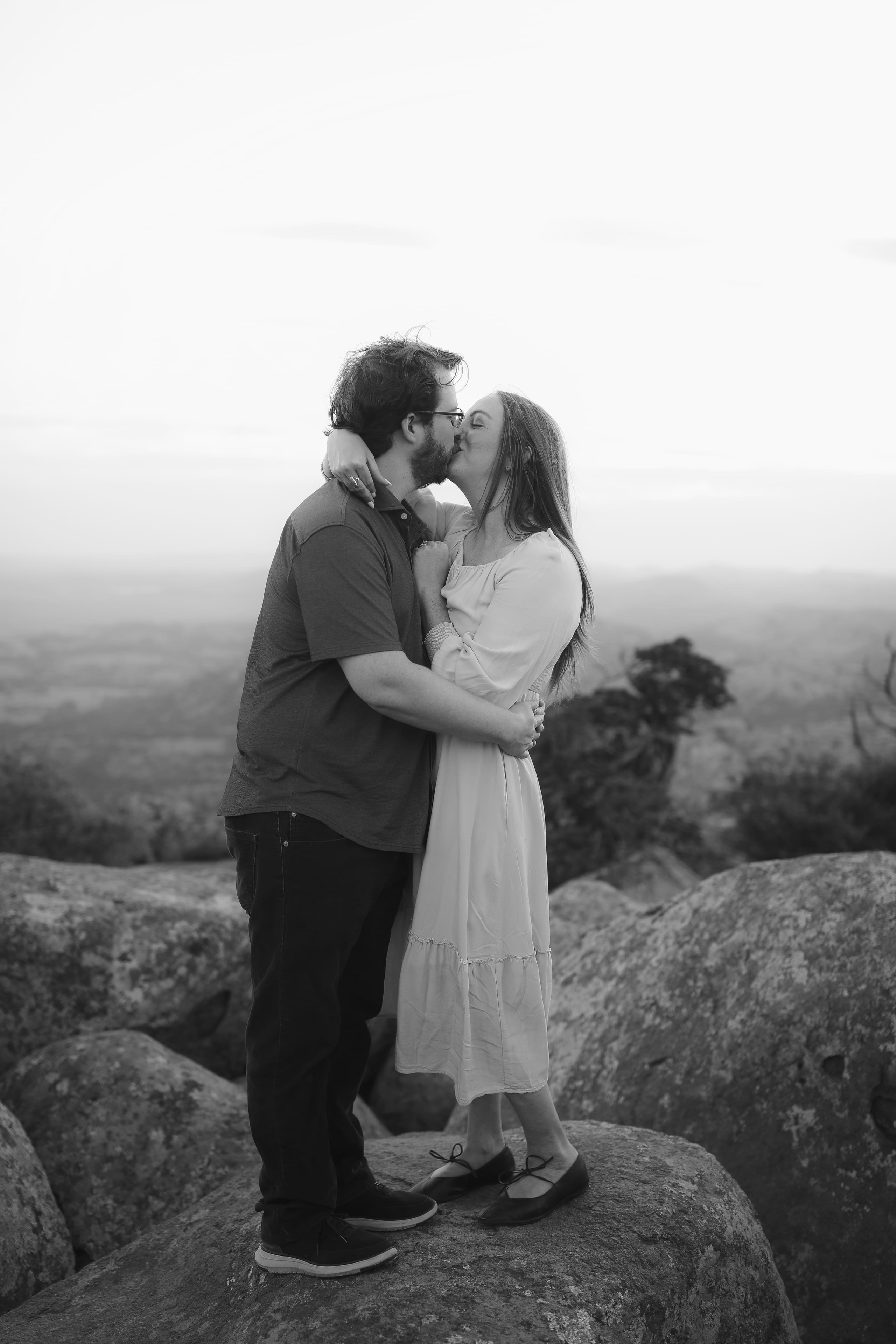 A kiss on the granite summit, the valley soft and pale behind them