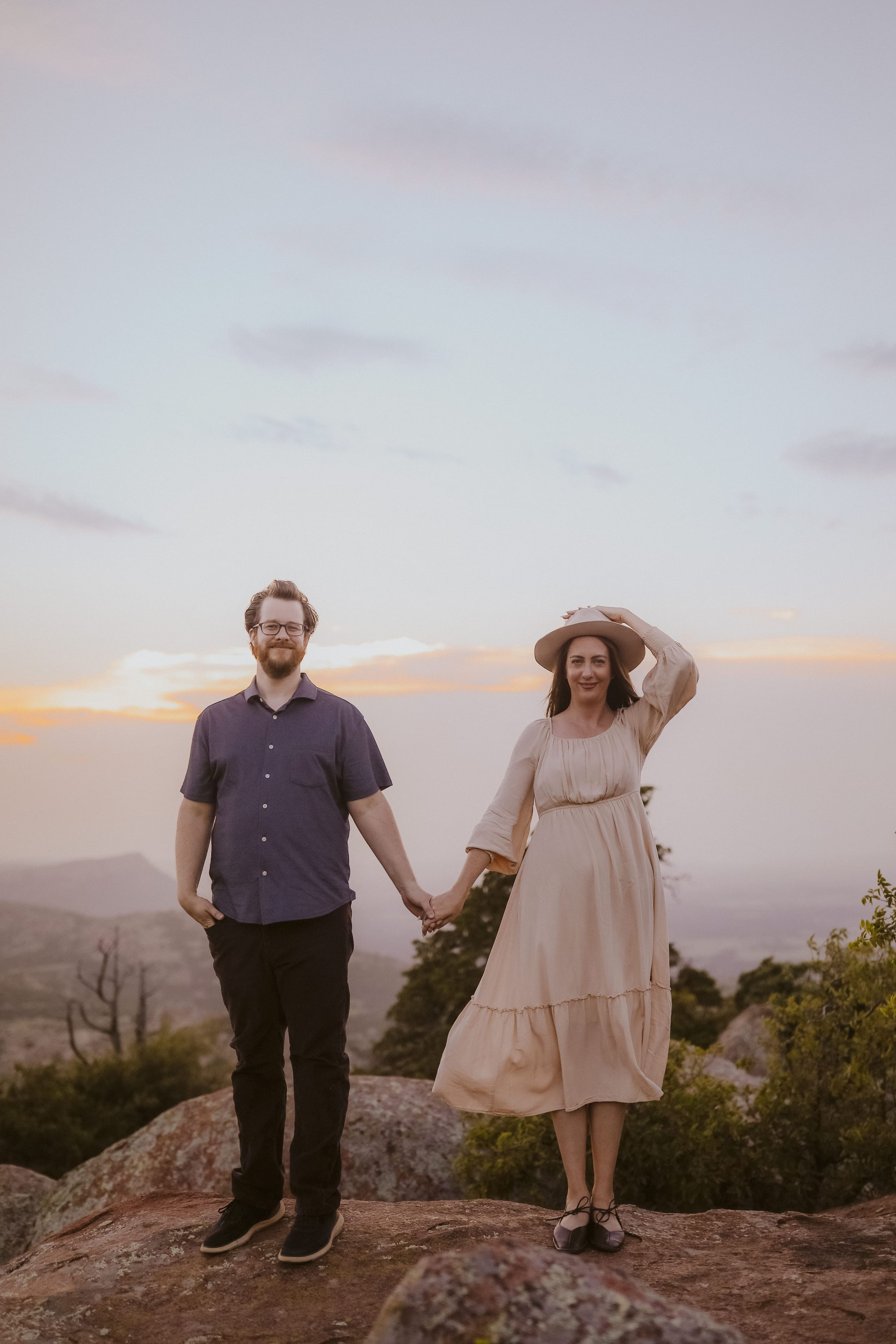 Hand in hand on the mountaintop, she holds her hat against the wind