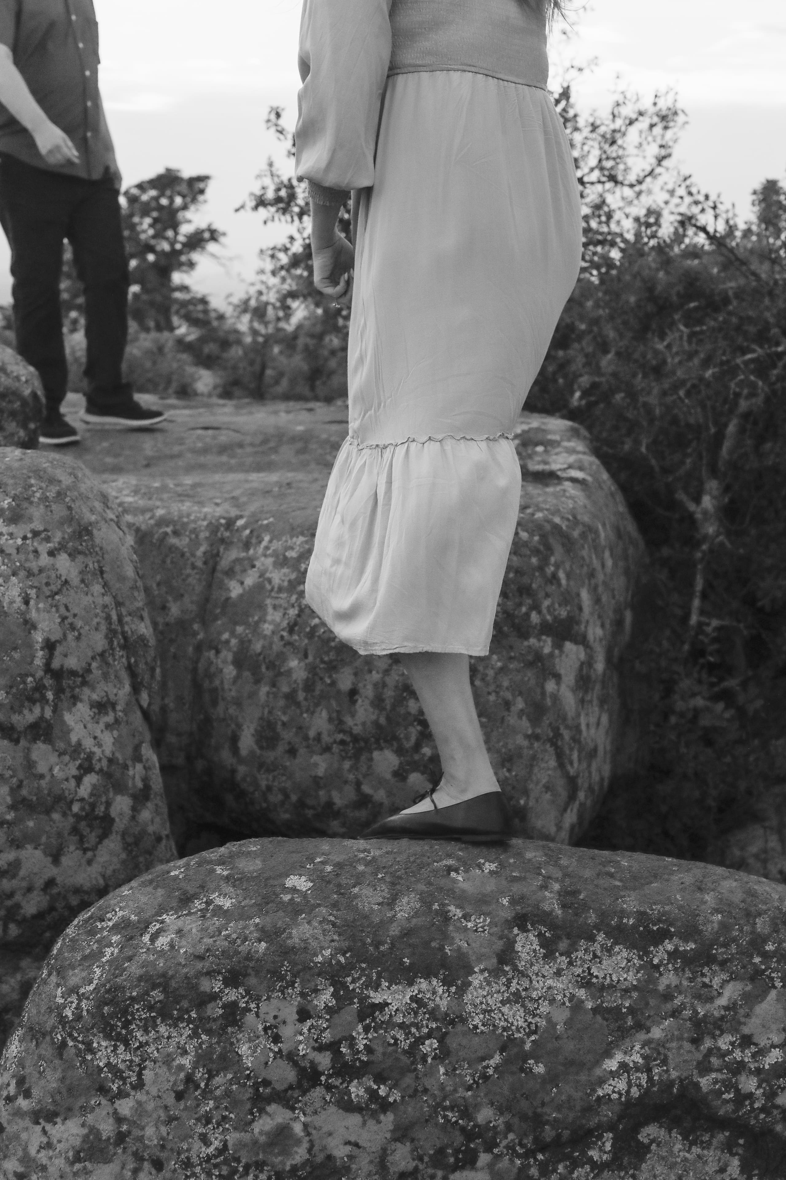 A quiet detail in black and white — her dress and flats crossing the boulders