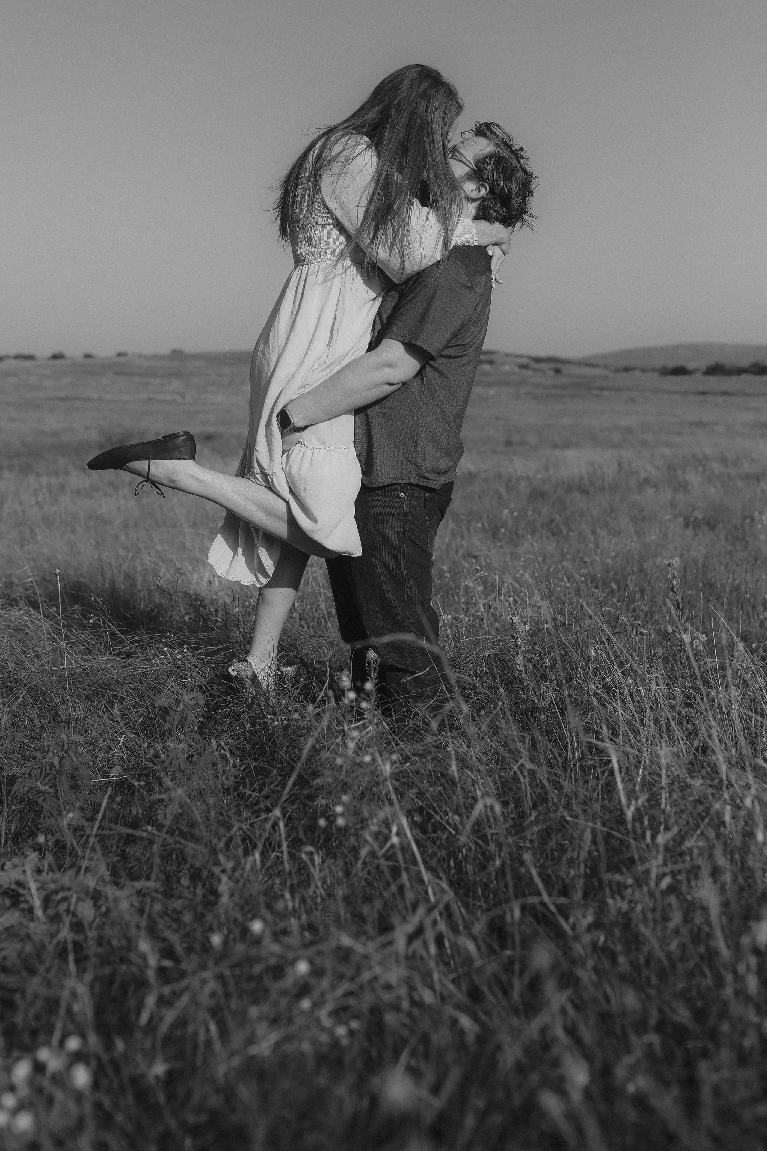 A kiss mid-lift in the tall grass, in black and white